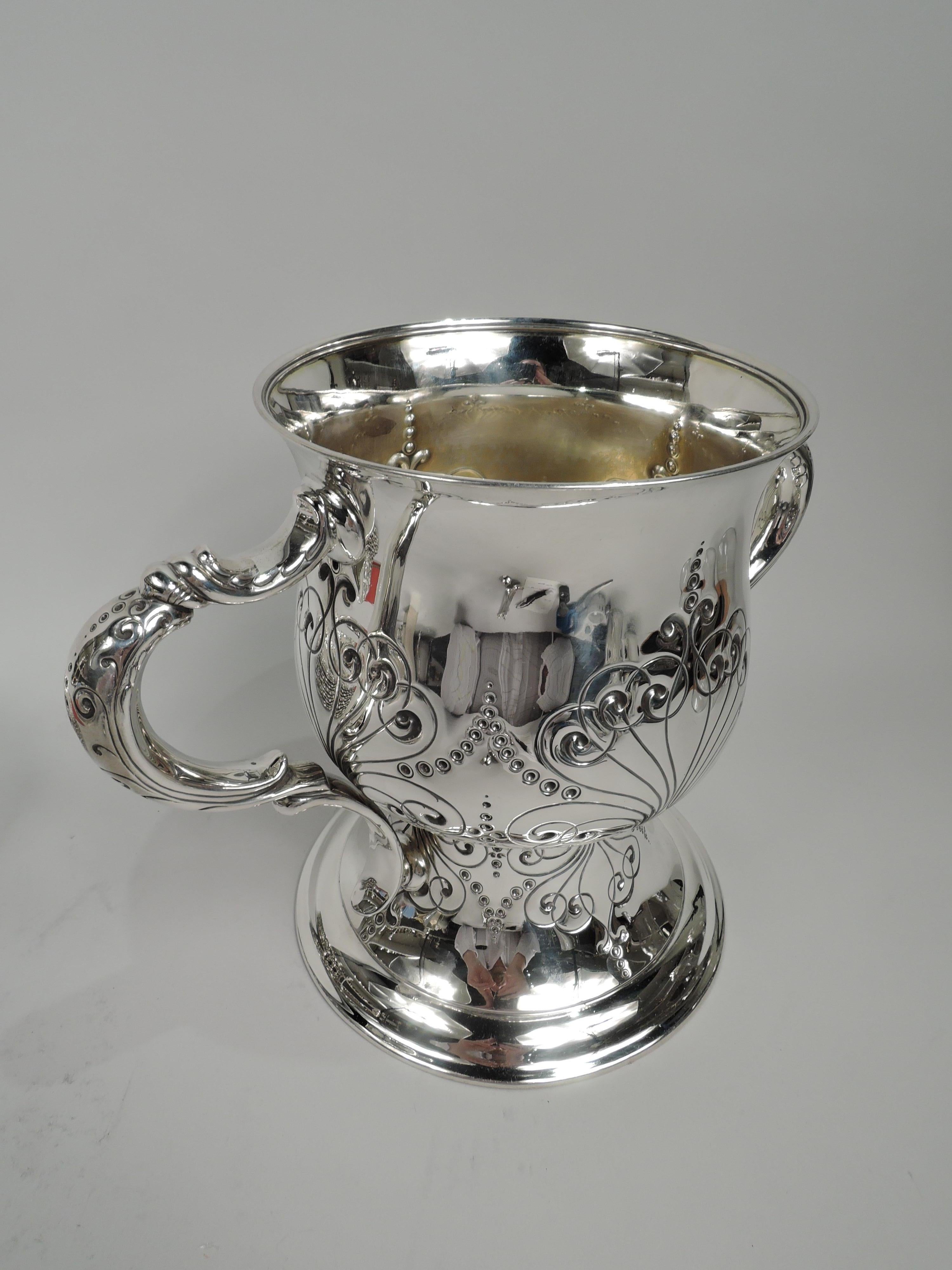 Art Nouveau sterling silver trophy cup. Made by Tiffany & Co. in New York. Urn on tall and spread foot; double-scroll side handles. Chased semi-abstract tendrils terminating in volute scrolls, garlands, and pendant flowers. A fluid, slightly