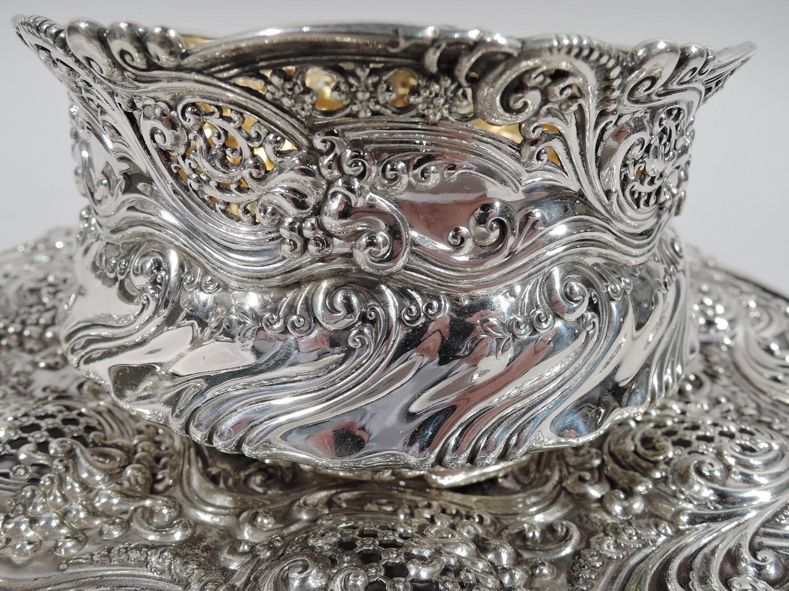 Sterling silver bowl on plate made by Tiffany & Co. in New York. Bowl: Squat with wavy and flared rim and short scrolled foot with bracket supports. Gilt interior. Plate: Round with scalloped rim. Plain and deep wavy star well with chased scrolls at