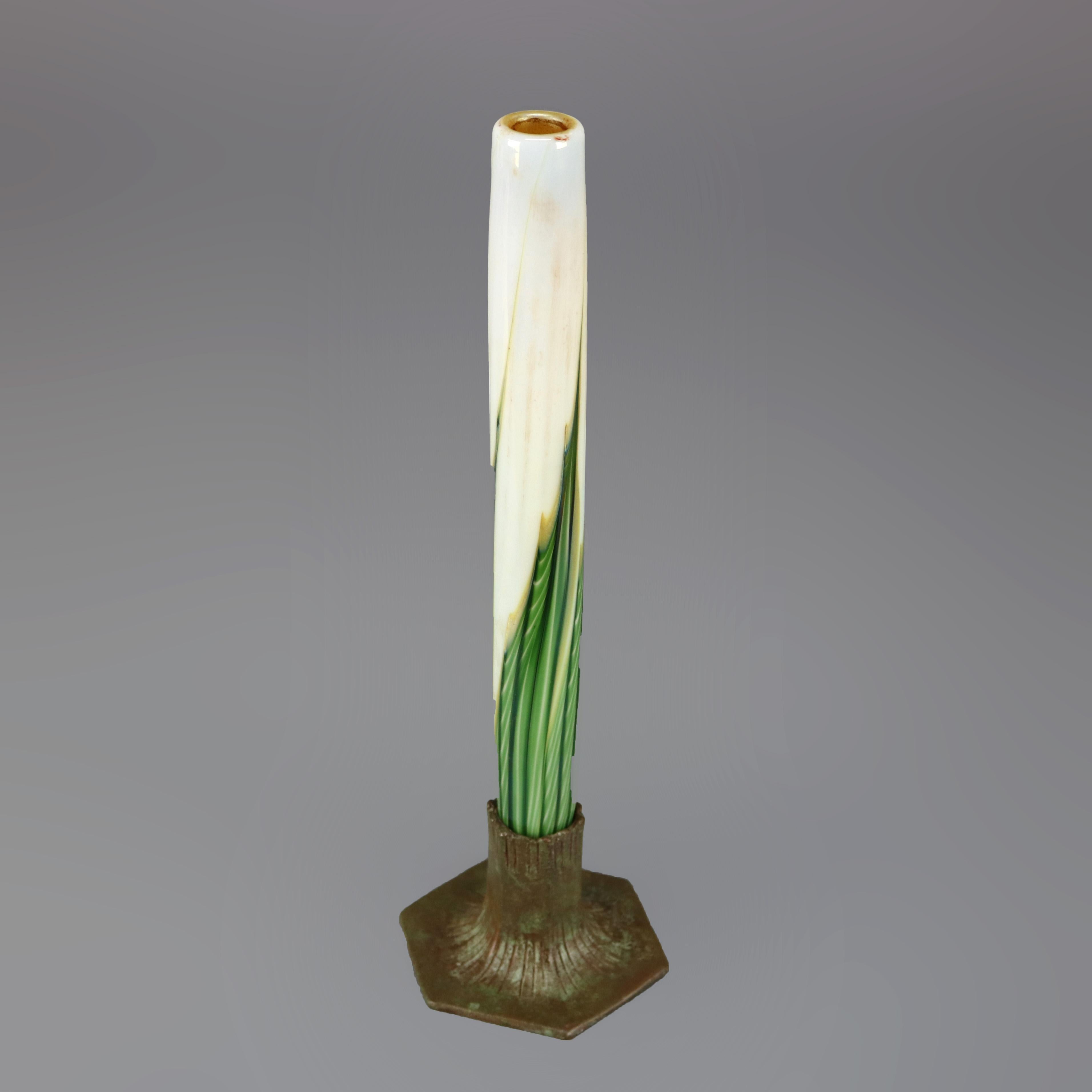 An antique bud vase in the manner of Tiffany offers art glass cylindrical vessel with green, gold and white pulled feather design, gold wash interior and seated in scored cast bronze base with hexagonal foot, base later added stamp as photographed,
