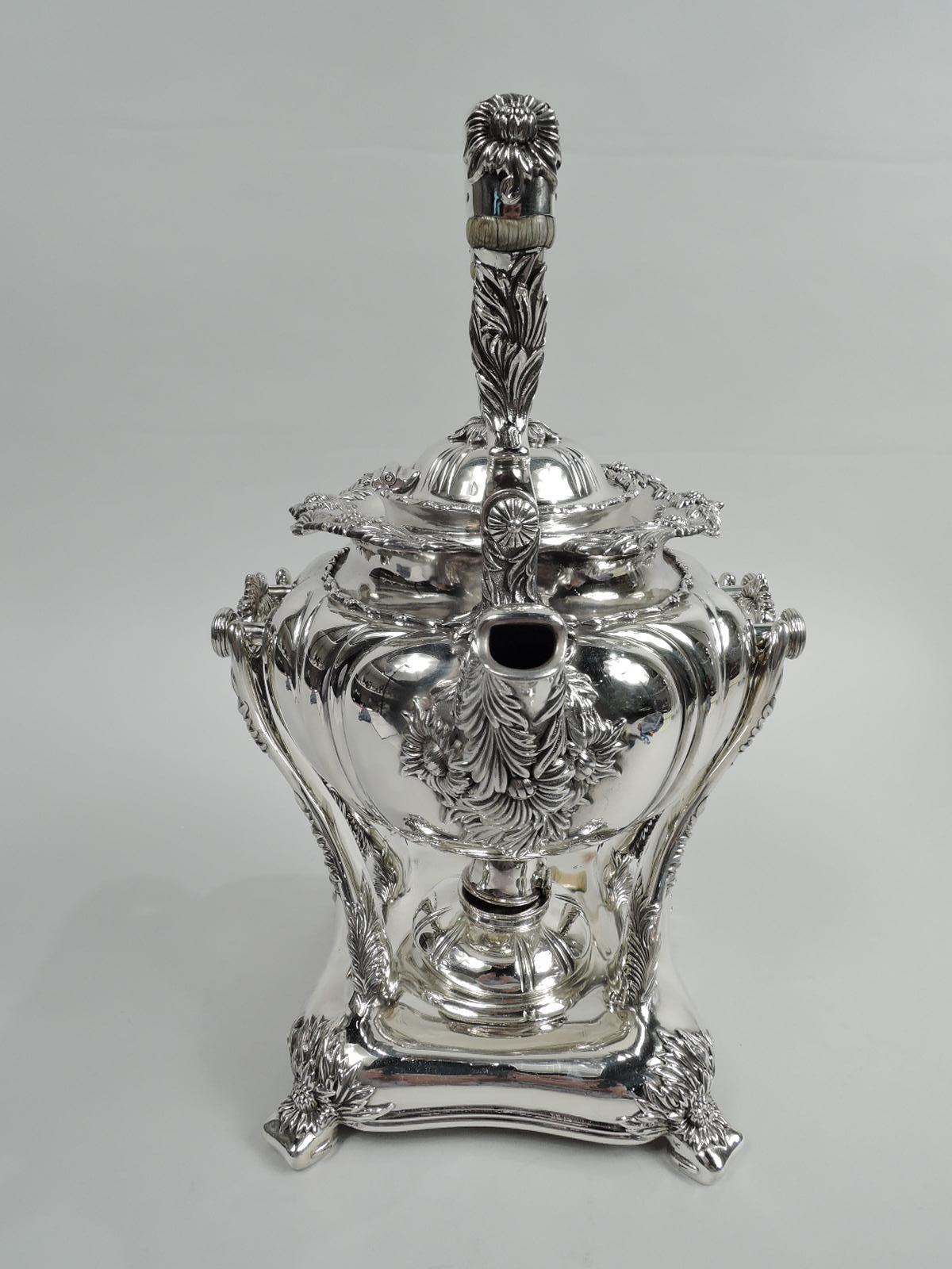 Chrysanthemum sterling silver tea kettle on stand. Made by Tiffany & Co. in New York. Round with tooled scrolls forming frames. Wavy rim applied with alternating flower-head and leaf pattern. Denser and less orderly bunches wrapped around tapering