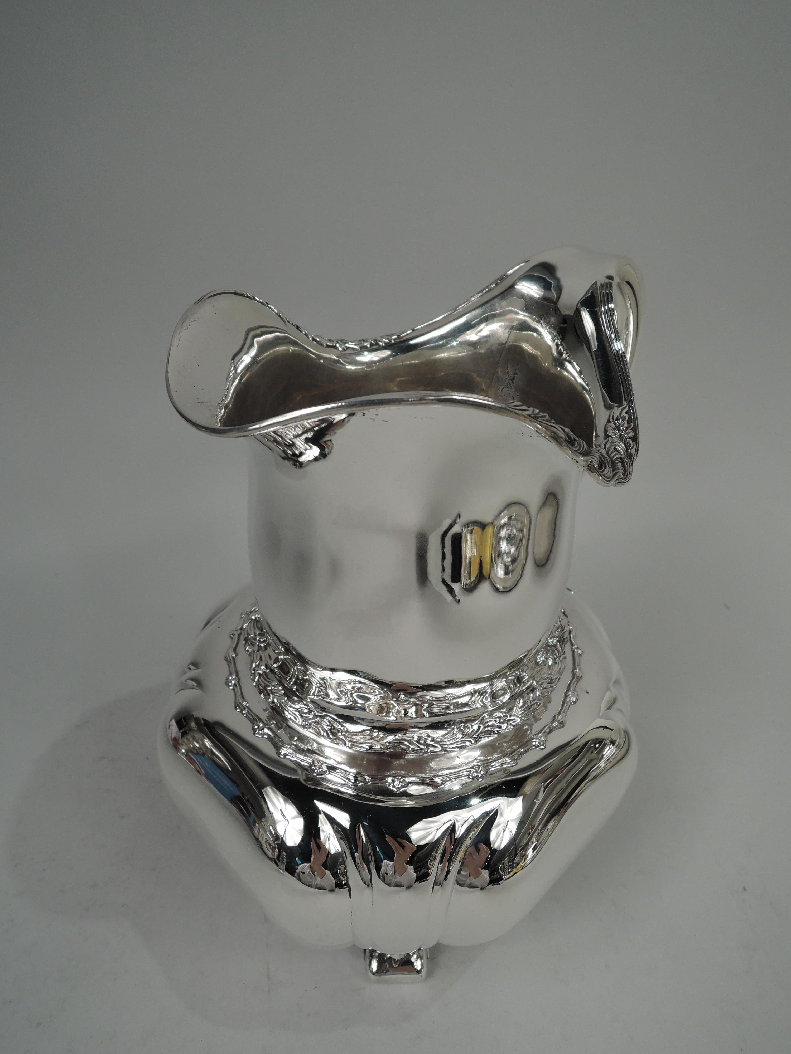 Chrysanthemum sterling silver water pitcher. Made by Tiffany & Co. in New York. Rectilinear shaped bowl with embossed flared tendrils at corners. Gently curved neck and helmet mouth with turned-down rim and scroll handle. Four flat volute supports.