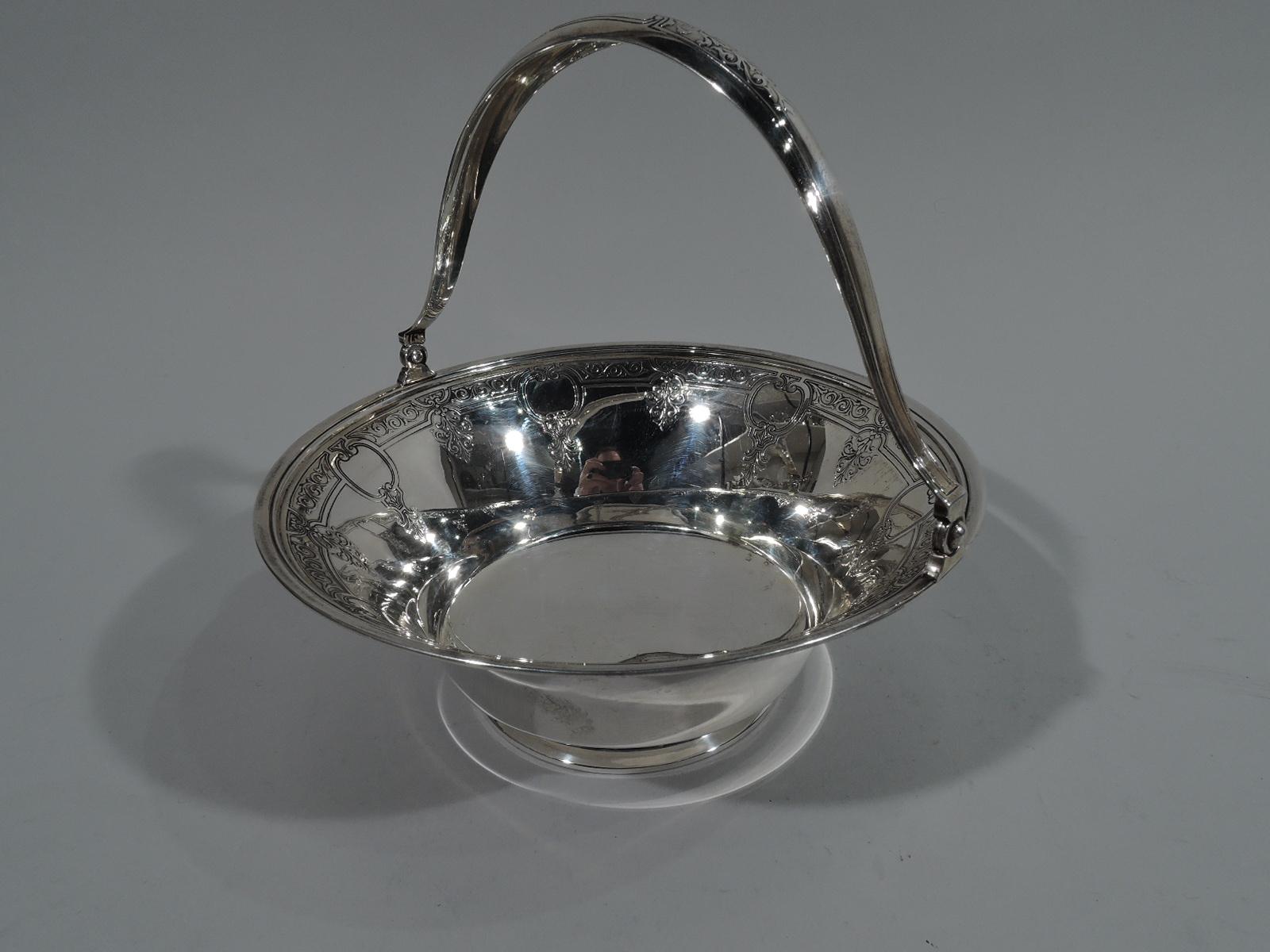 Classical sterling silver basket. Made by Tiffany & Co. in New York, circa 1915. Round and wide with tapering sides, raised foot, and bell-form swing handle. Acid etched ornament. On inerior scrolled border interspersed with alternating palmettes