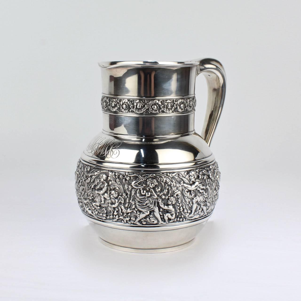 A very fine Tiffany & Co. Olympian Sterling Silver water pitcher.

Of bulbous form with a wide band of chased cherubs and deities amid foliate scrolls and the neck chased with a band of foliate scrolls. The front bears a large cursive monogram.

The