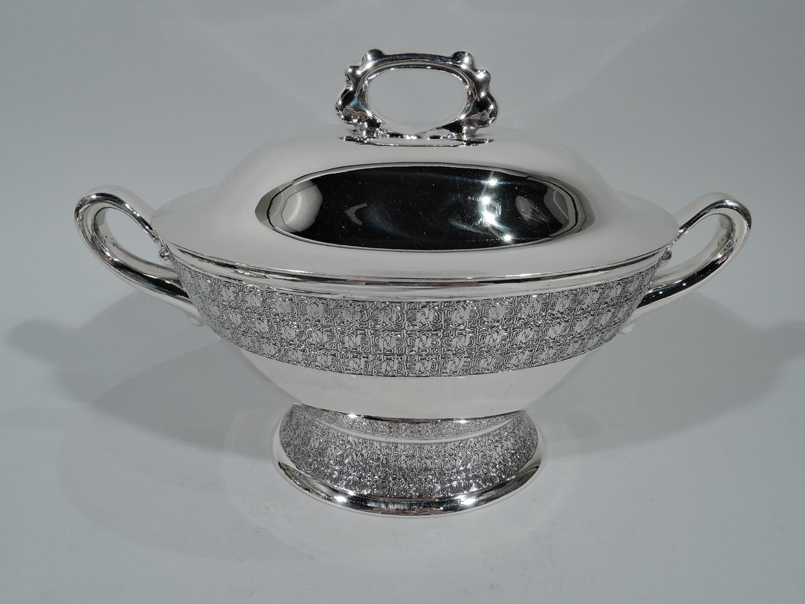 Stylish sterling silver tureen. Made by Tiffany & Co. in New York. Ovoid bowl, looping end handles with graduated “drips”, and raised and spread foot. Raised cover with notched ring finial. Dense and fluid fretwork bands. A late Victorian design
