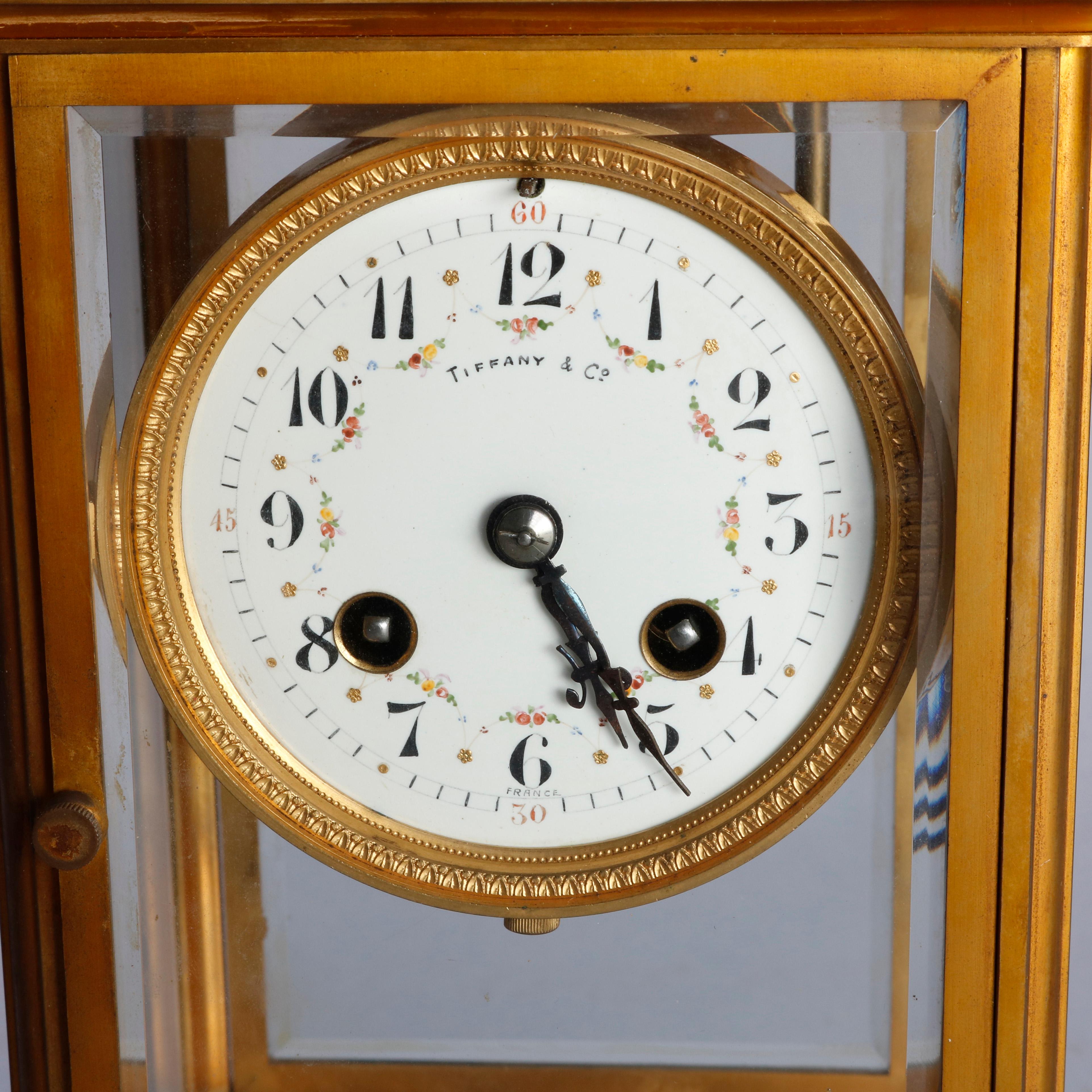 An antique crystal regulator mantel clock by Tiffany & Co. offers case having brass and beveled crystal case raised on bracket feet, works with porcelain face having Arabic numbers and floral garland highlights, signed as photographed and inscribed