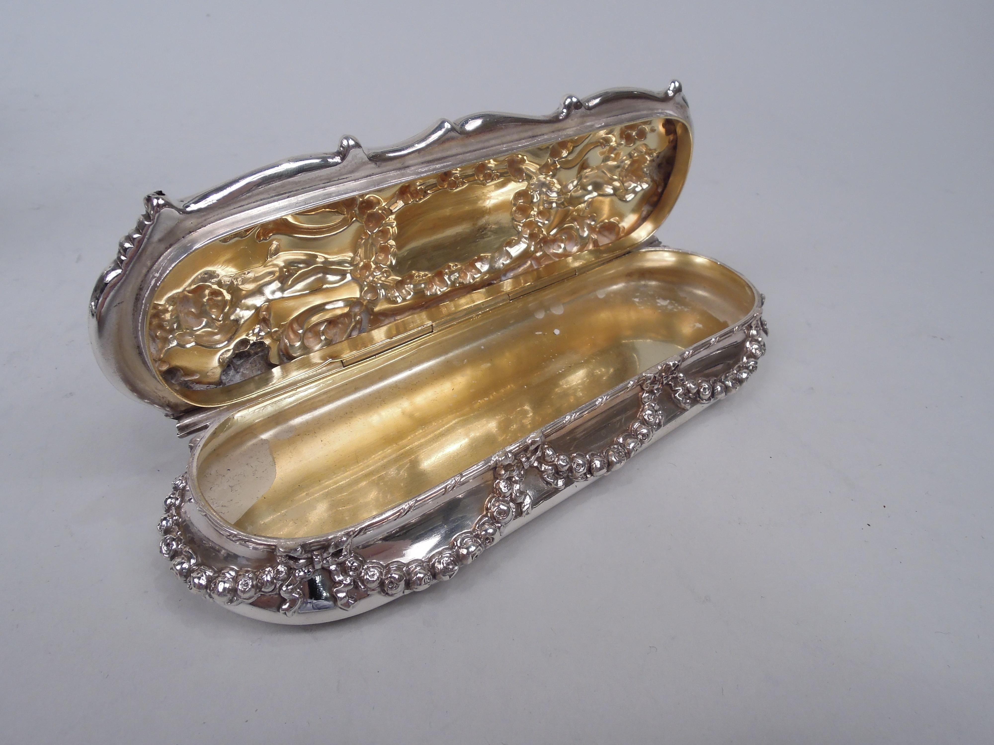 Edwardian Classical sterling silver trinket box. Made by Tiffany & Co. in New York. Oval with upward tapering sides and hinged scrolled cover. On sides applied ribbon-tied garland. On cover top chased scrolls threaded with garlands overlapping