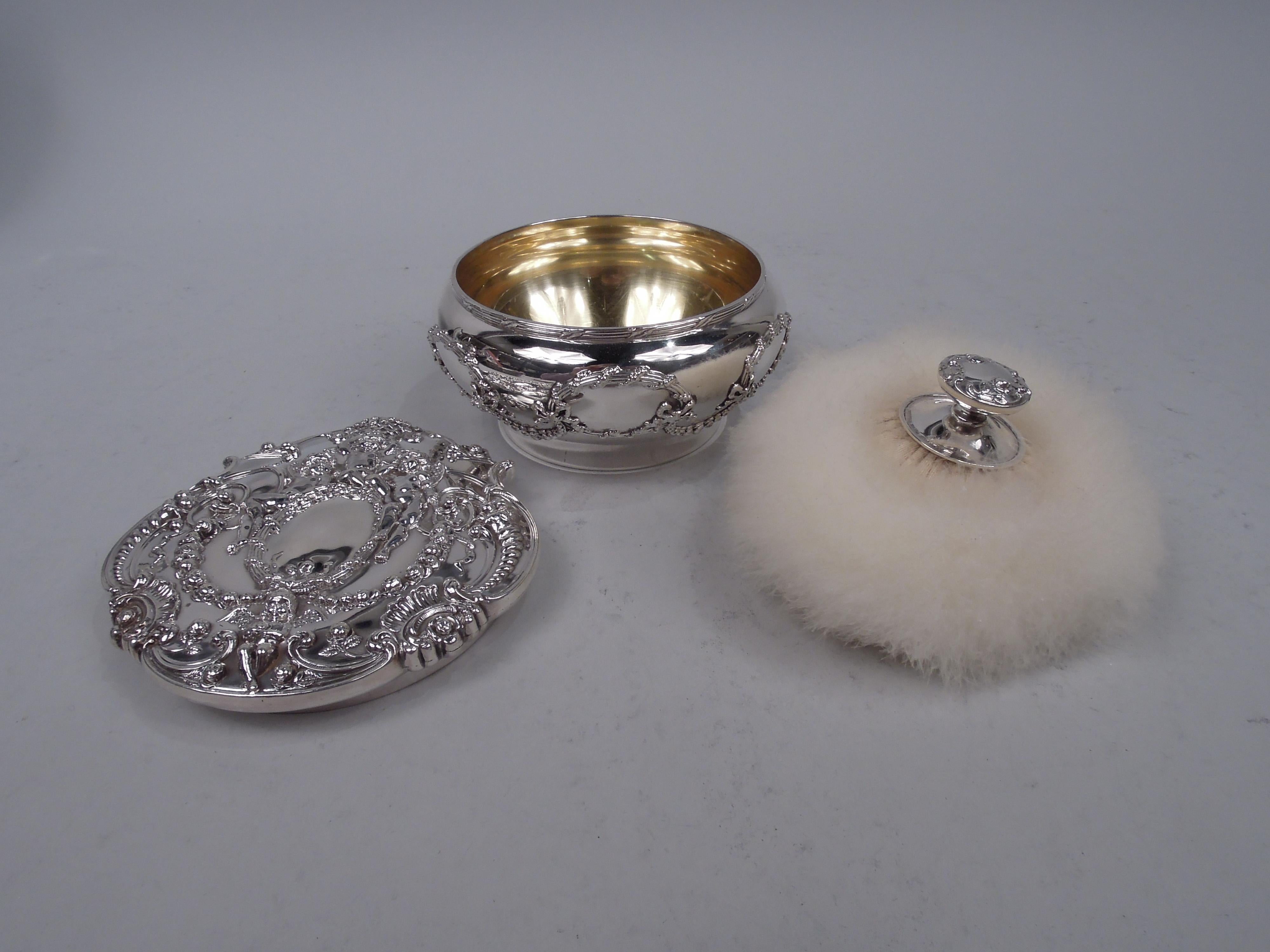 Edwardian Classical sterling silver powder box. Made by Tiffany & Co. in New York. Round and bellied with flat and scrolled cover. Chased and applied ornament. On bowl oval reeded frames joined by pendant garlands. On cover central same frame