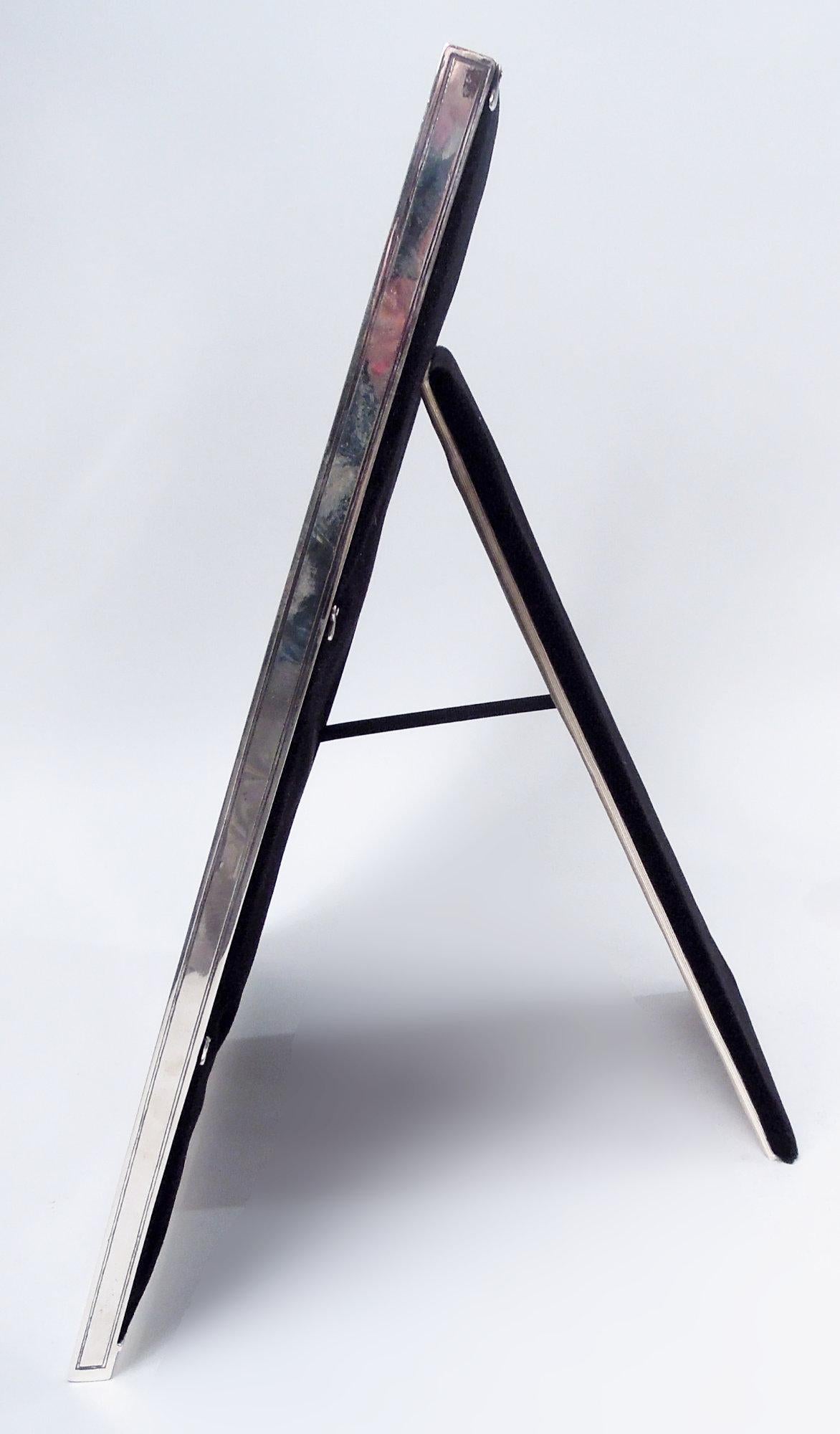 Edwardian Classical sterling silver table mirror. Made by Tiffany & Co. in New York, ca 1910. Beveled oval class set in rectangular frame. On front, acid-etched entwined leafing scrollwork at corners and border comprising tubular frames with