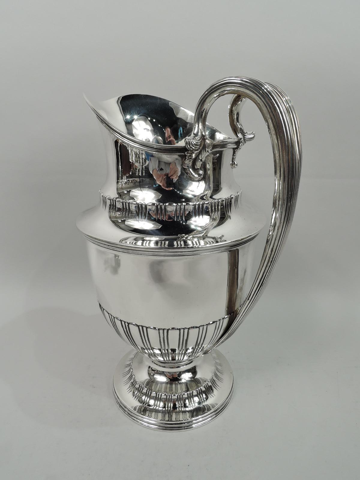 Edwardian classical sterling silver water pitcher. Made by Tiffany & Co. in New York. Helmet mouth and ovoid body on raised and round foot. Chased and incised stylized lobed borders. High-looping reeded handle with split and leaf-mounted top. Fully