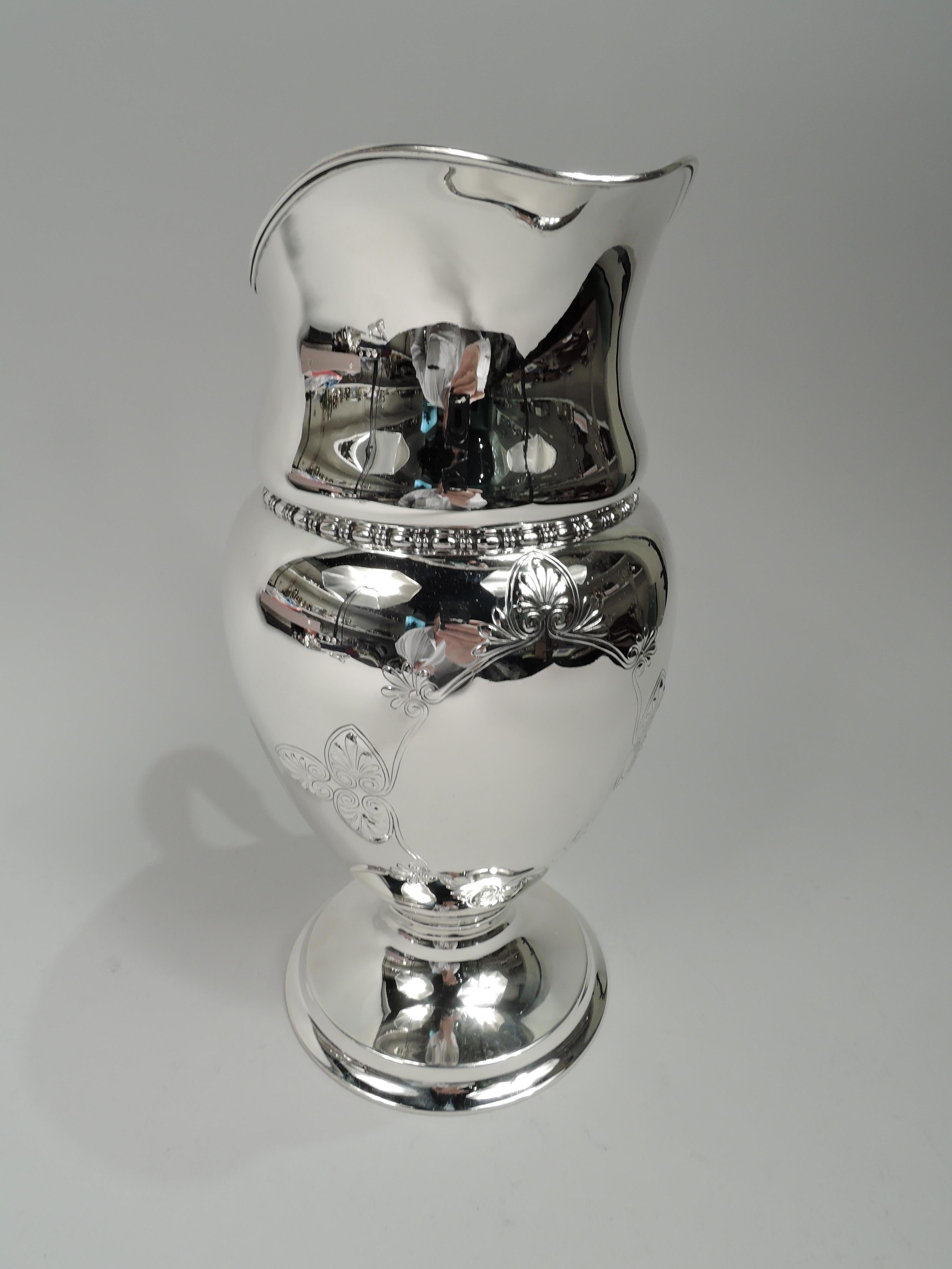 Edwardian Classical sterling silver water pitcher. Made by Tiffany & Co. in New York. Oval body on raised round foot. High-looping handle and helmet mouth. Chased oval frame with palmettes and acanthus leaves. Bead-and-reel border. Fully marked