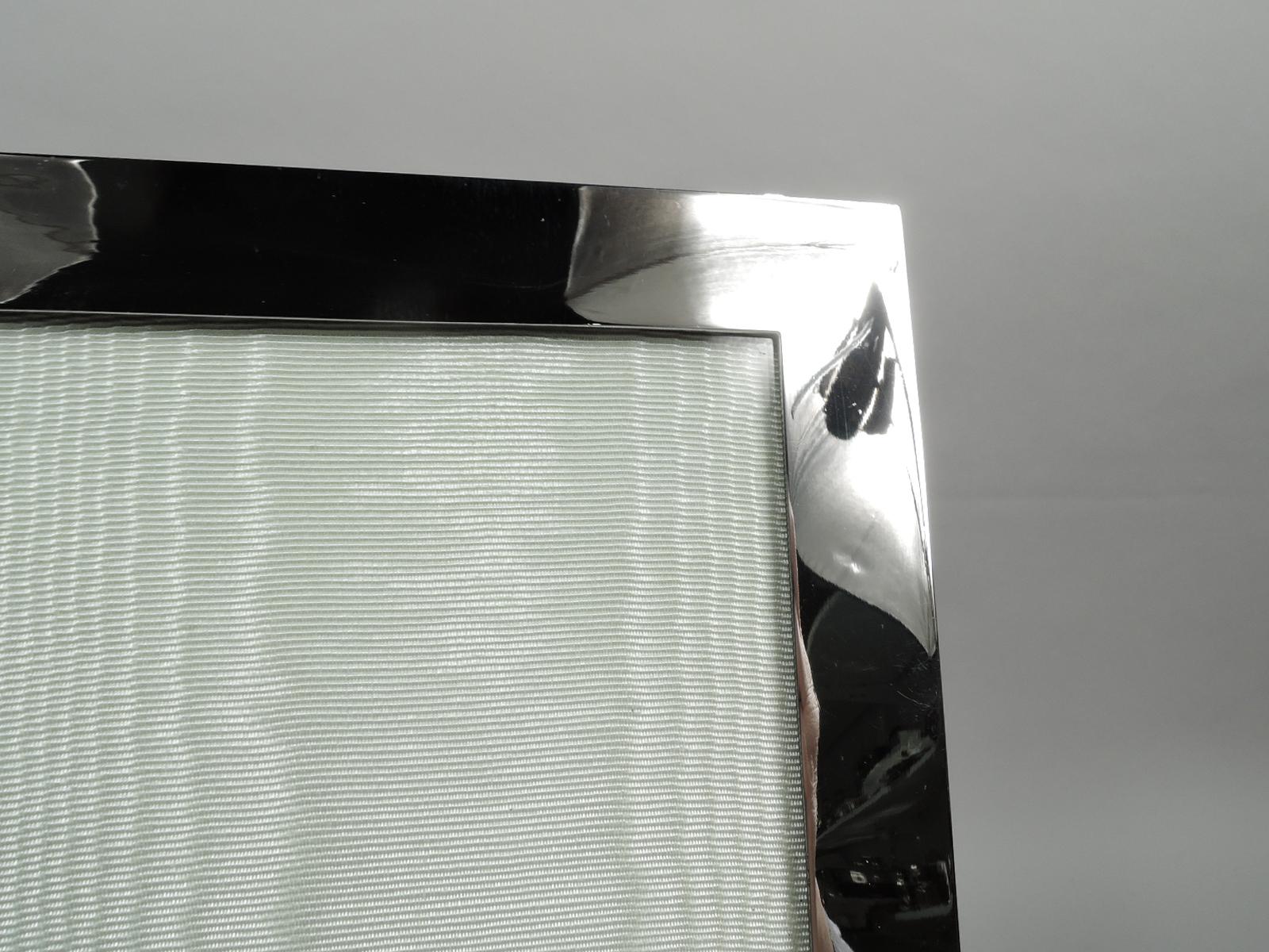 Cadre photo moderne édouardien en argent sterling. Fabriqué par Tiffany & Co. à New York, ca. 1910. Fenêtre rectangulaire dans un encadrement plat et uni. Avec verre, doublure en soie, dos en velours et support de chevalet à charnière. Entièrement