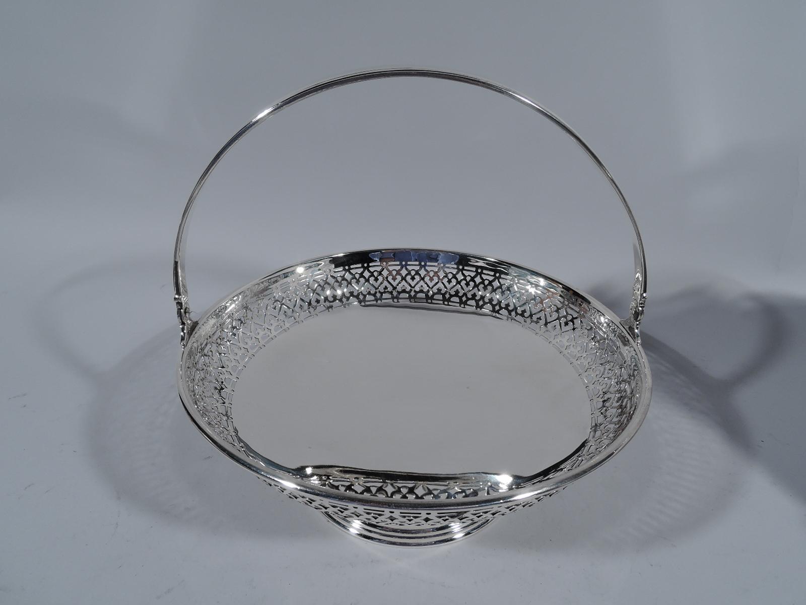 Edwardian sterling silver basket. Made by Tiffany & Co. in New York, circa 1912. Round and shallow bowl with solid well and wide band of pierced scrollwork. C-scroll handle tapering and hinged. Stepped and raised foot. Fully marked including pattern