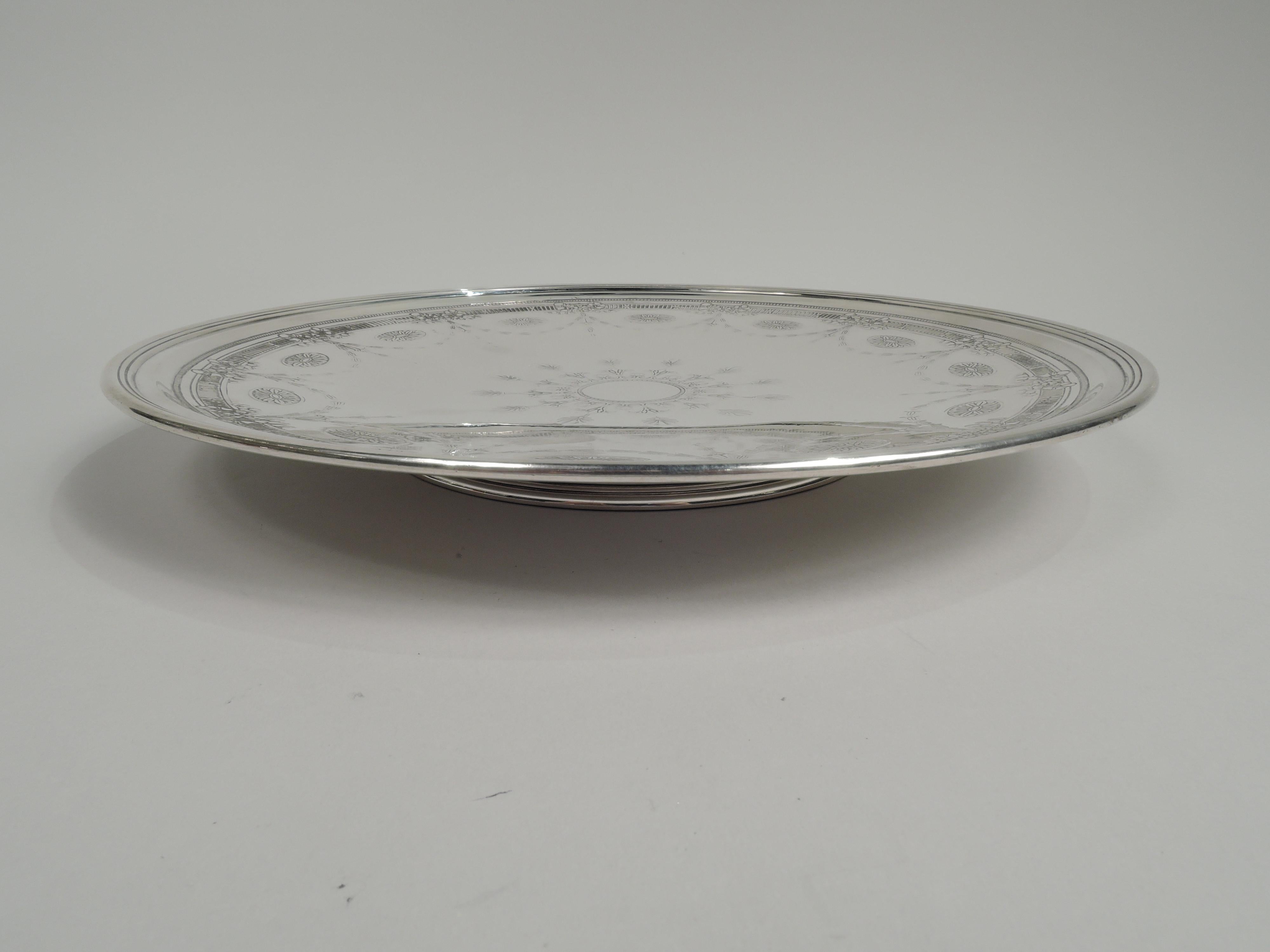 Edwardian Regency sterling silver cake plate. Made by Tiffany & Co. in New York, ca 1914. Round and shallow with reeded rim and round and stepped inset foot. Acid etched ornament: Dentil and fluted borders and pendant swags inset with paterae.