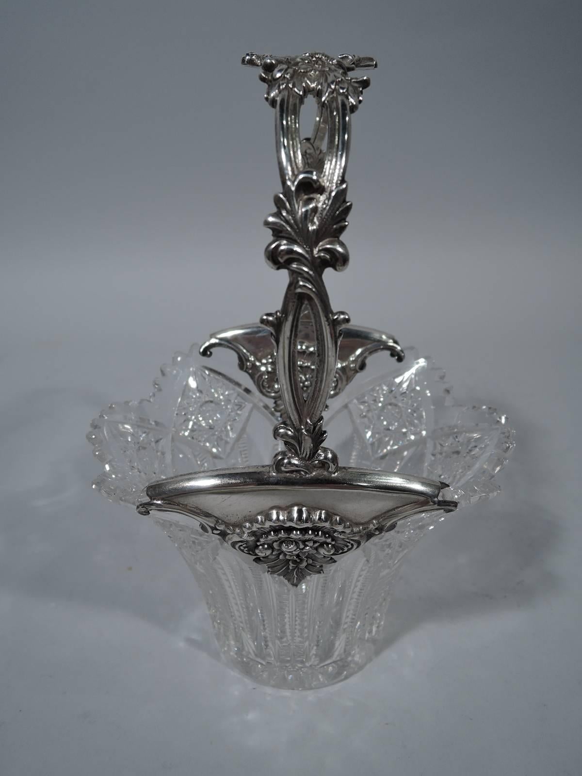 Brilliant-cut-glass basket with sterling silver mounts and handle. Made by Tiffany & Co. in New York, circa 1900. Circular well with tapering sides and ovalish mouth. Ornament includes flutes, notches, and stars. Scalloped rim. Mounts triangular