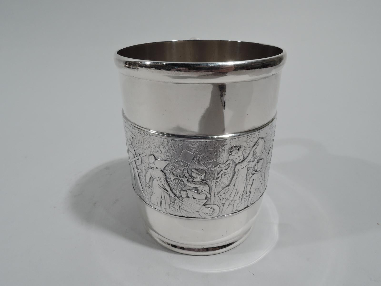 Victorian sterling silver baby cup. Made by Tiffany & Co. in New York. Straight sides and lobed c-scroll handle. Low-relief frieze of children’s parade—a boisterous procession of boys and girls blowing bugles, jangling tambourines, and beating