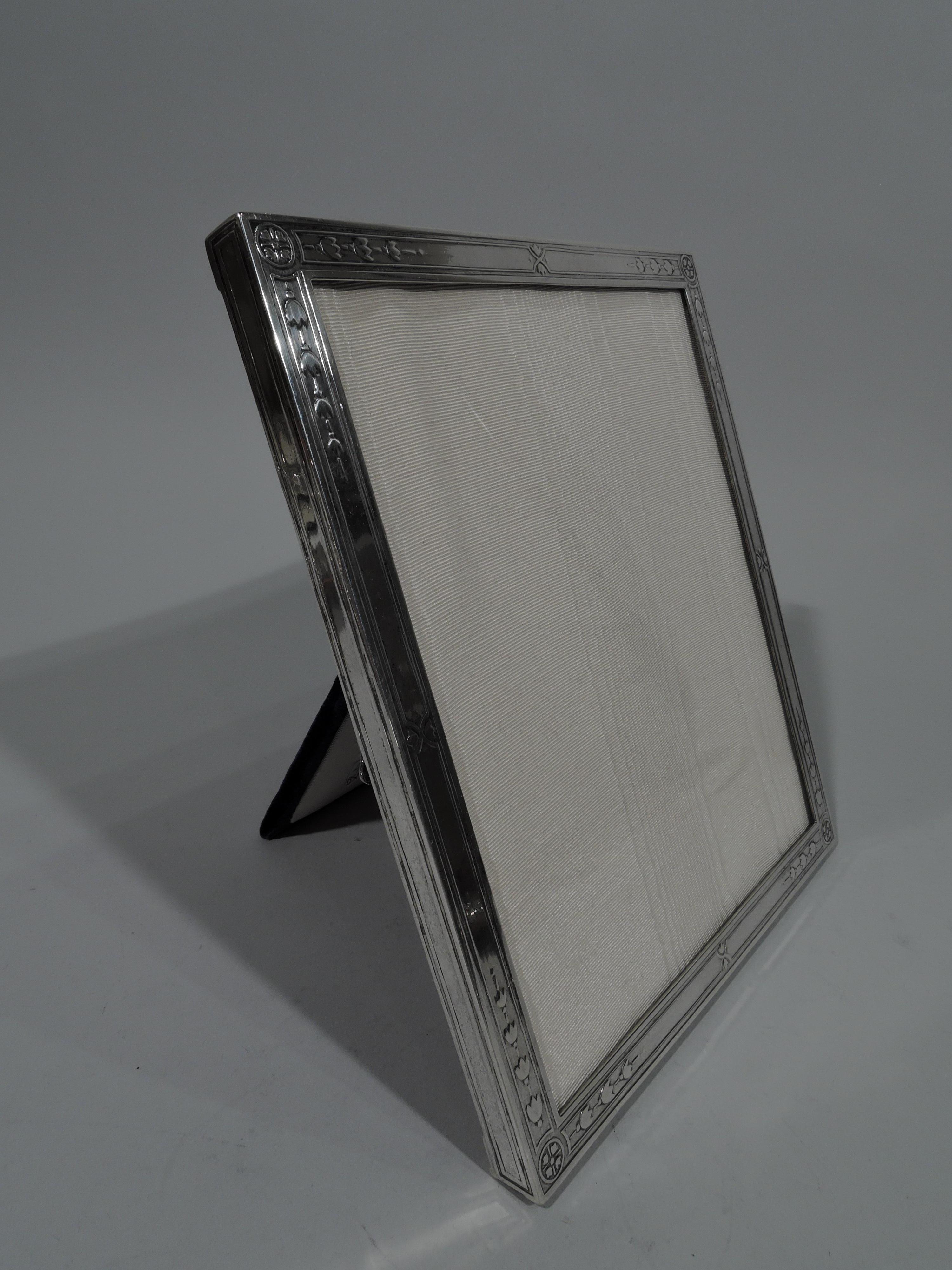 Edwardian sterling silver picture frame. Made by Tiffany & Co. in New York, circa 1910. Rectangular window and flat surround with acid-etched ornament: Stylized flowers in rectilinear frames and corner paterae. Sides have same frames. With glass,