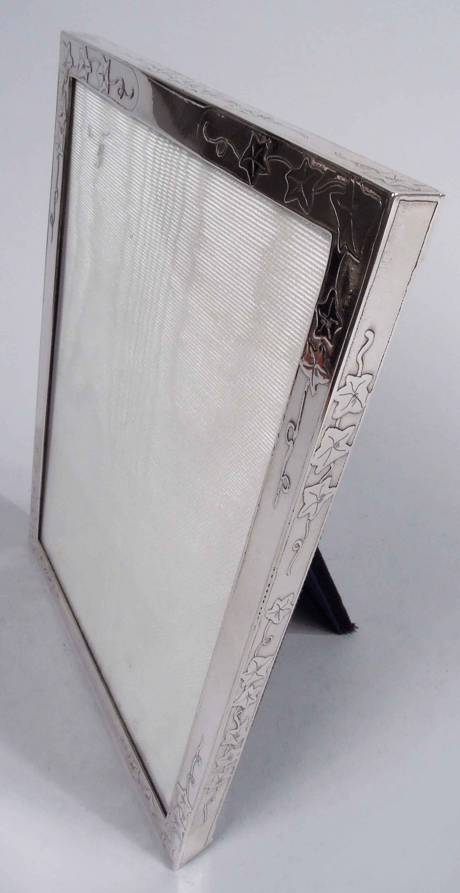 Edwardian sterling silver picture frame. Made by Tiffany & Co. in New York, ca 1910. Rectangular window in same flat surround. Acid-etched meandering ivy on front and sides. With glass, silk lining, and velvet back and hinged easel support for