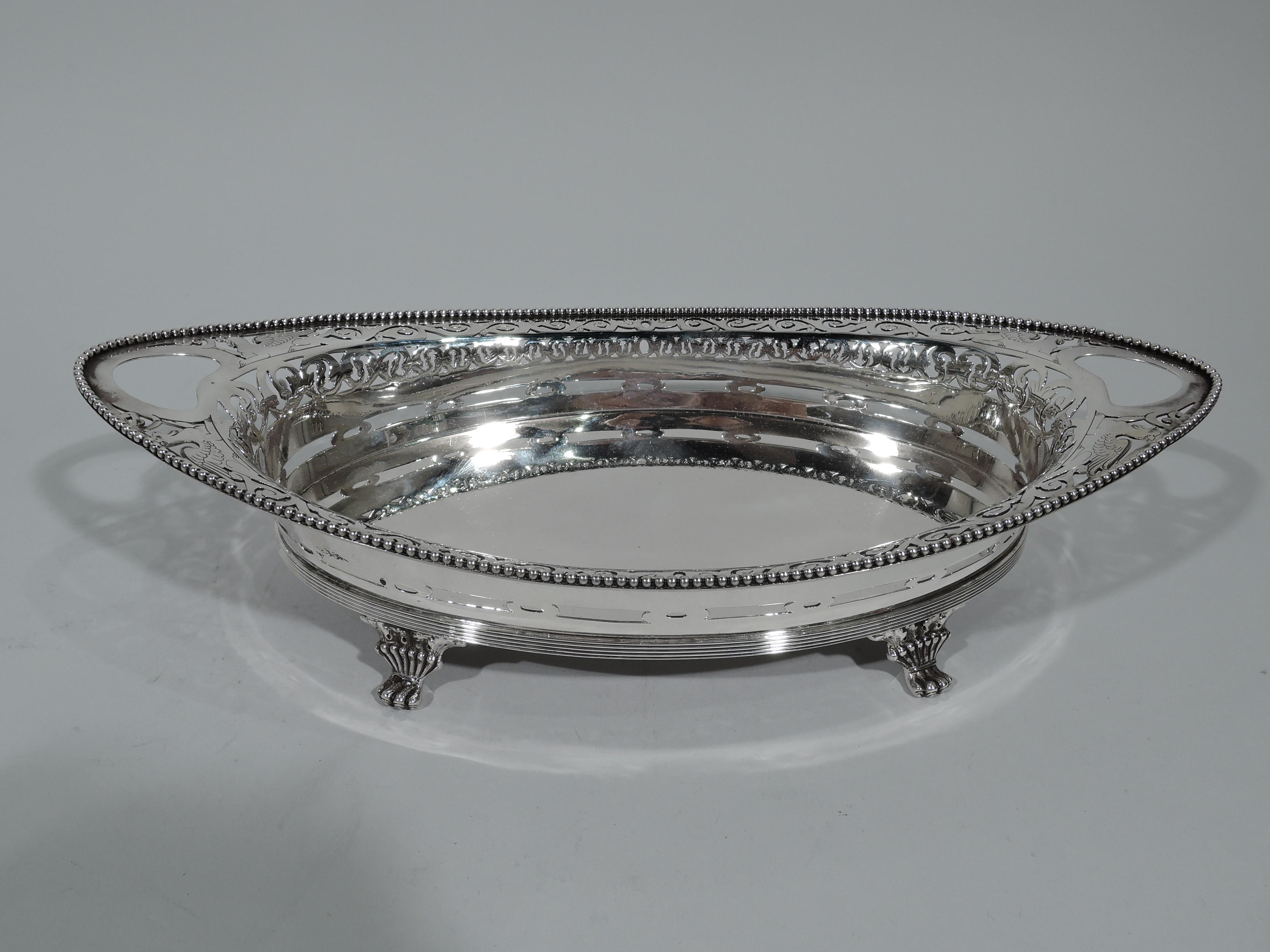 Neoclassical sterling silver bread tray. Made by Tiffany & Co. in New York. Solid oval well. Sides have pierced ornament including gryphons and rinceaux. Cutout kidney end handles and beaded rim. Reeded base and 4 leaf-mounted paw supports. Hallmark