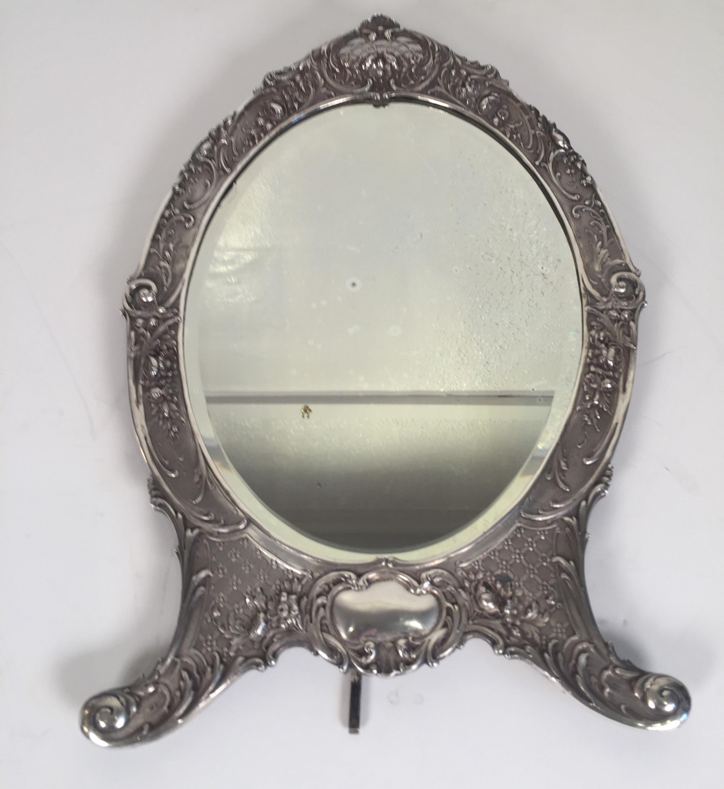Sterling silver vanity mirror. Made by Tiffany in New York, circa 1900. The oval form with floral and scroll motif all-over the frame, the hand beveled oval glass is original. The back with original velvet backing. Marked on the frame with Tiffany