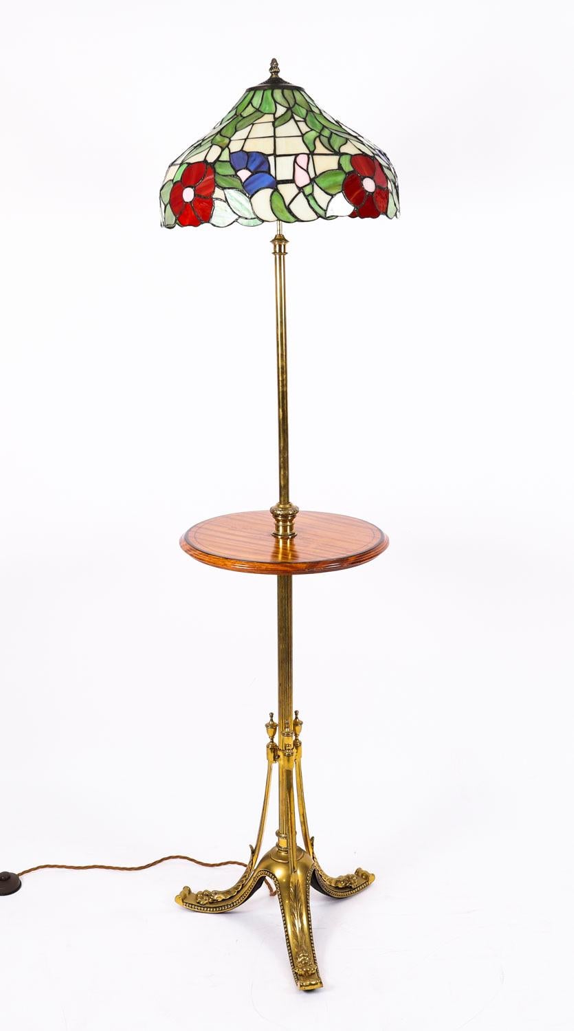 Elegante lámpara de pie telescópica de principios del siglo XX, de cristal emplomado, madera satinada y ormolu, de estilo renacimiento Tiffany.

El esbelto fuste acanalado se eleva sobre tres columnas en forma de 