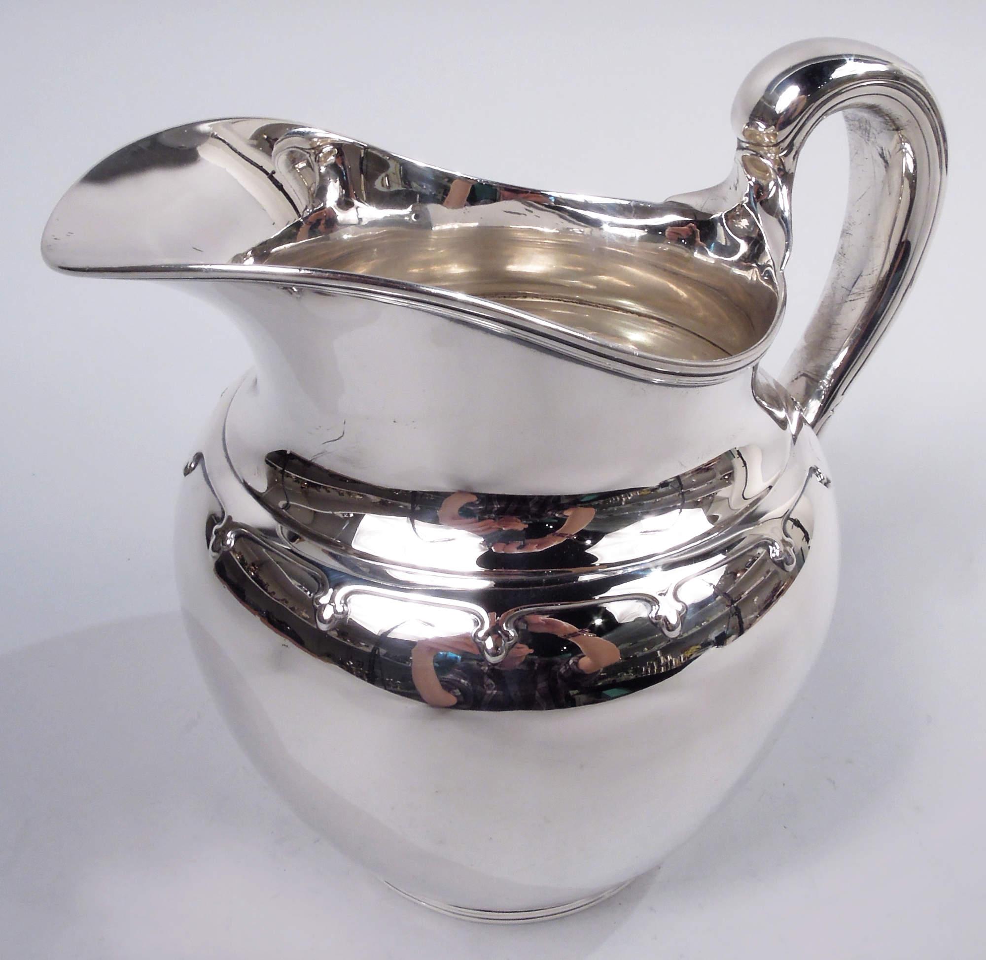 Saint Dunstan sterling silver water pitcher. Made by Tiffany & Co. in New York, ca 1910. Globular with high-looping and capped handle, helmet mouth, and reeded foot ring. Girdle with pendant fleurs de lys applied to shoulder. Fully marked including