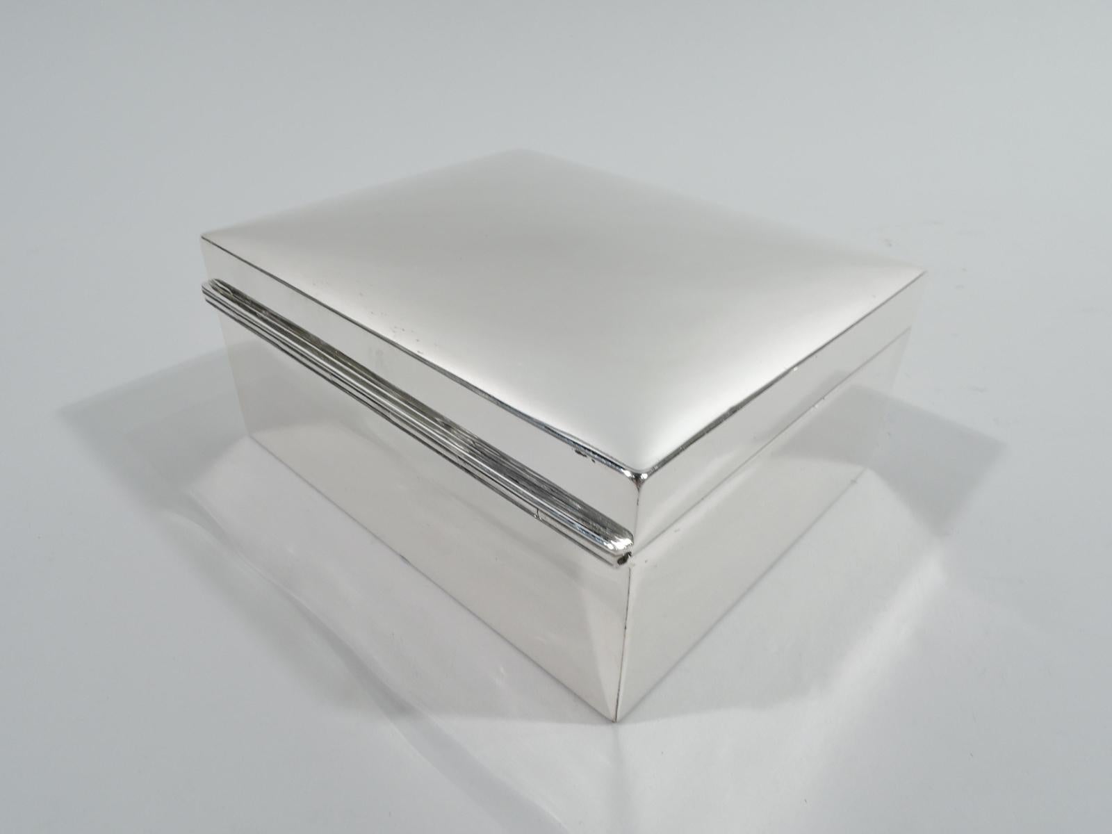 Small sterling silver jewelry box, ca 1910. Retailed by Tiffany & Co. in New York. Rectangular with straight sides. Cover hinged and raised with gently curved top and tapering tab. Fitted velvet lining with detachable tray. With key. Marked “Tiffany