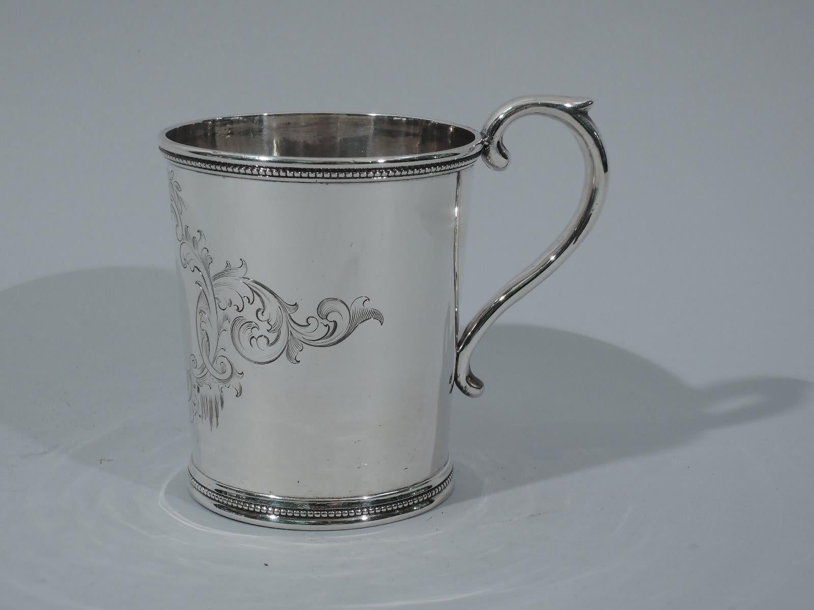 Early sterling silver baby cup. Made by Grosjean & Woodward for Tiffany & Co. at 550 Broadway. Straight and tapering sides and capped S-scroll handle. Beaded and molded rim and foot. Engraved cartouche (vacant) with fluid scrolls and flowers.
