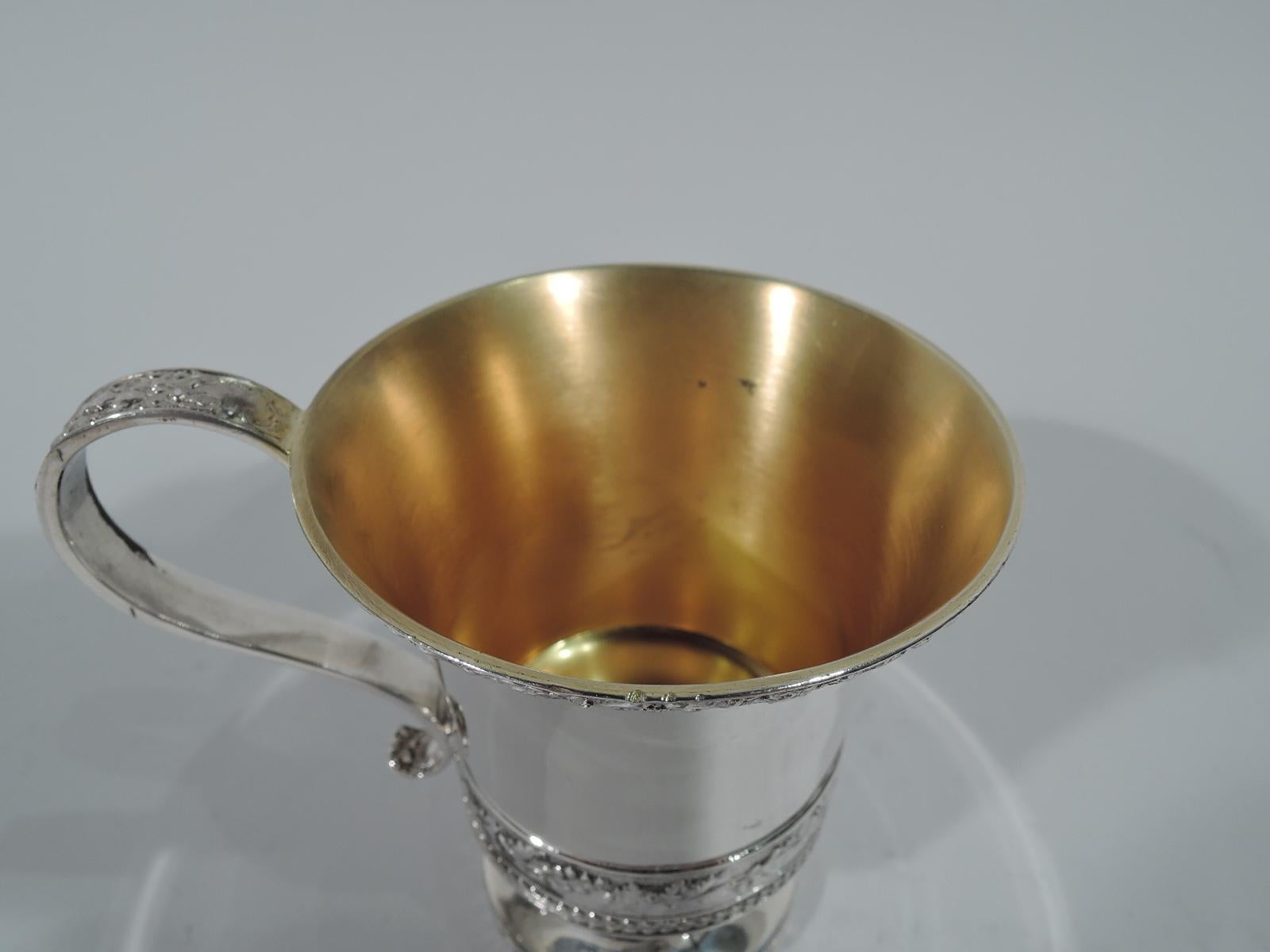 Sterling silver baby cup. Made by Tiffany & Co. in New York. Tapering bowl with flared rim, s-scroll handle, and raised foot. Tooled bands of flowers and foliage as well as fruiting berry branch. Gilt interior. Lots of room for engraving. Hallmark