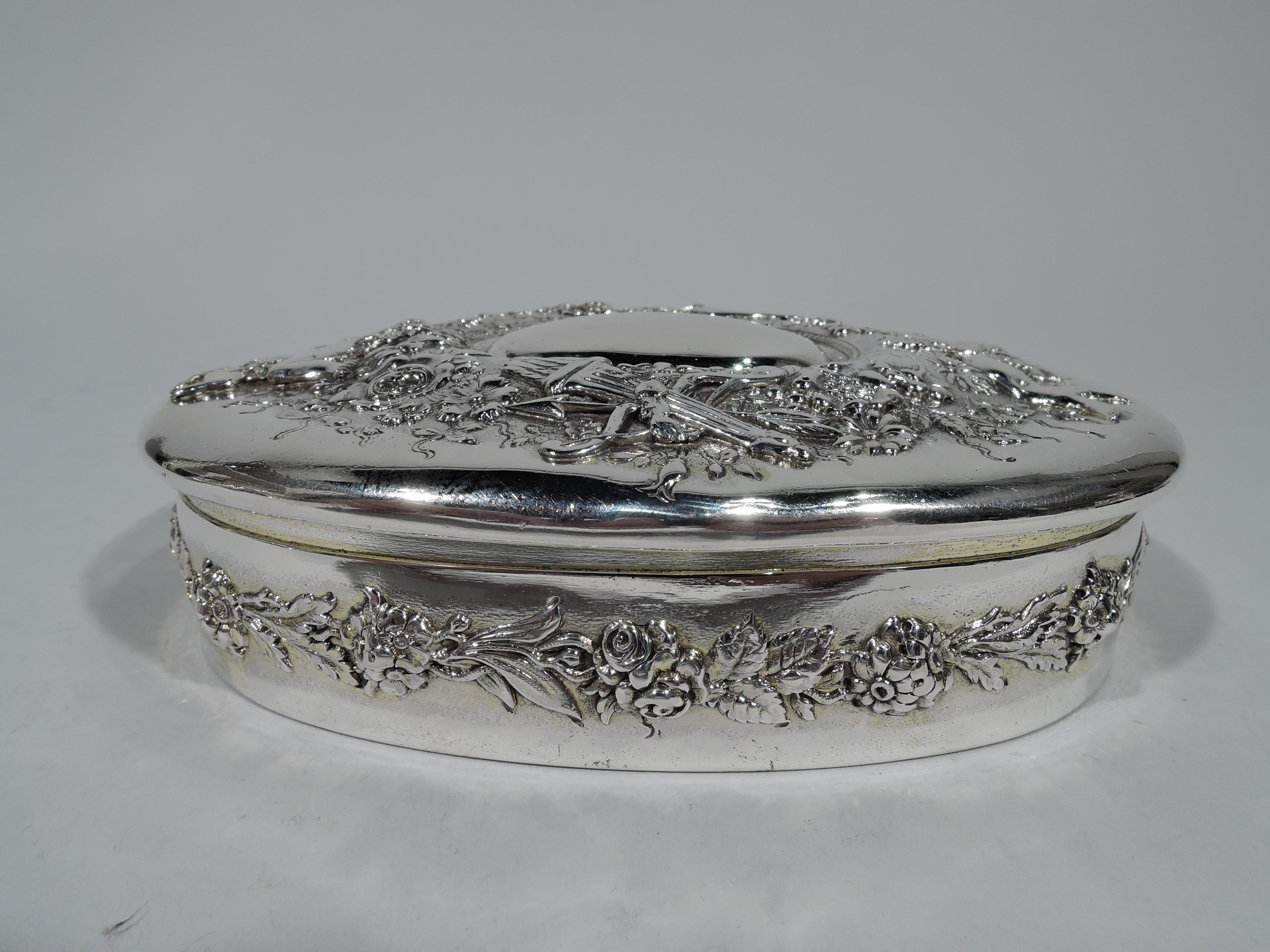 Romantic Victorian sterling keepsake box. Made by Tiffany & Co. in New York. Oval with floral garland on sides. Cover hinged with oval frame (vacant) surrounded by buck-naked Cupids entwined in dense floral garland as well as symbolically potent