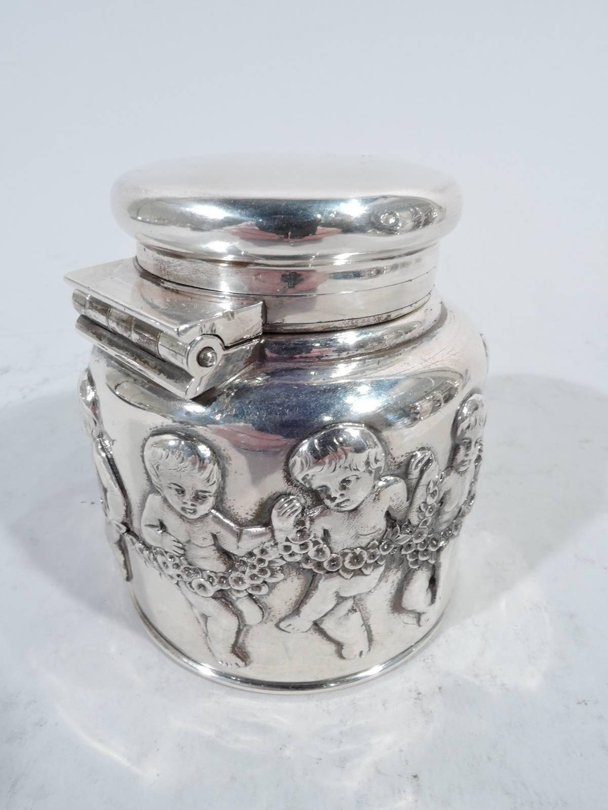 Sterling silver inkwell. Made by Tiffany & Co. in New York. Drum-form with hinged and cork-lined bayonet cover. Exterior encircled with charming chubby cherubs holding a strategically placed garland. Interior lined with clear glass. On underside is
