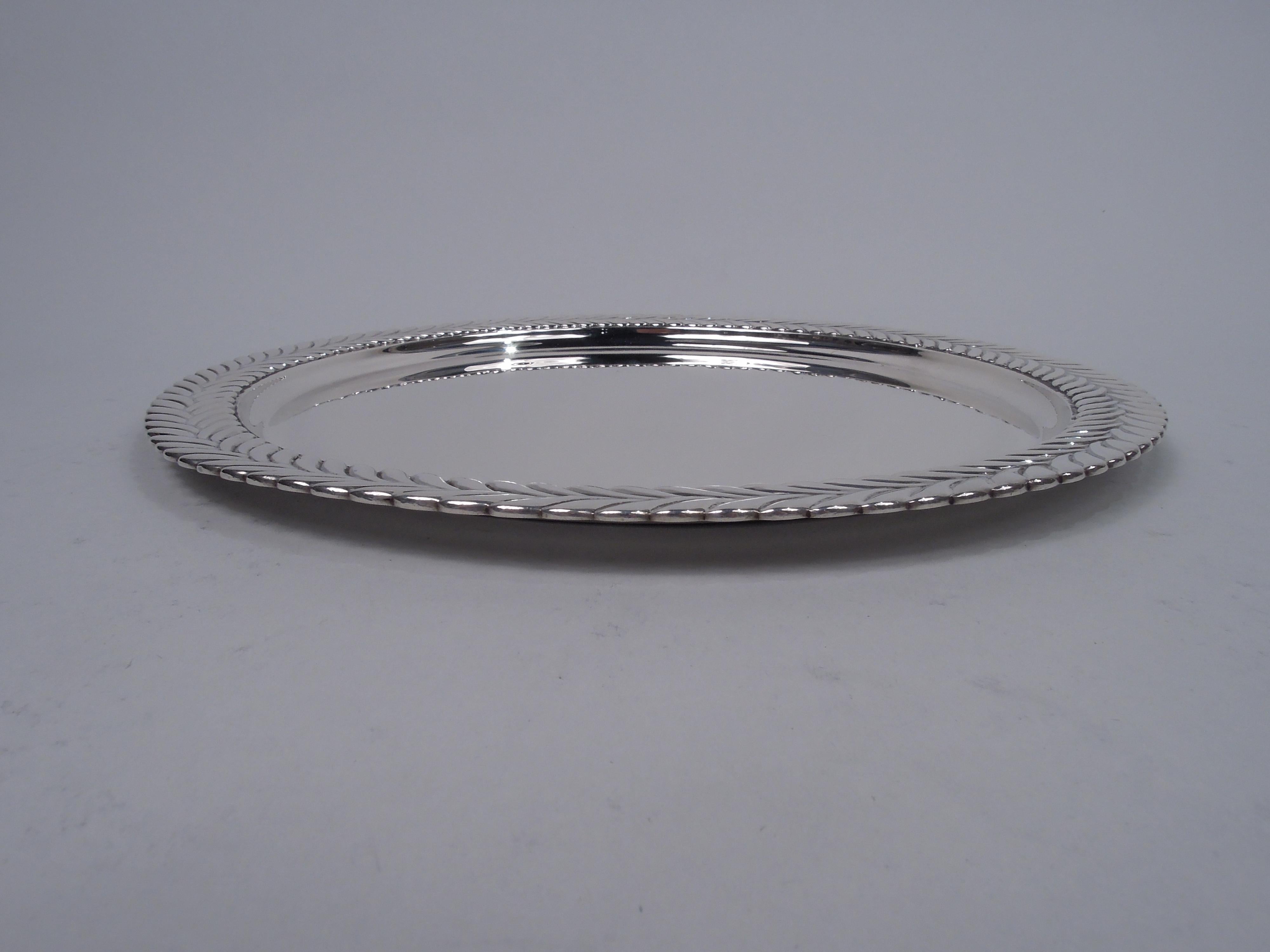 Stylish Victorian sterling silver tray. Made by Tiffany & Co. in New York. Round and plain well. Wide rim with low-relief border in form of imbricated leaves or chevrons. A popular motif that is sometimes known as Wave Edge. Fully marked including