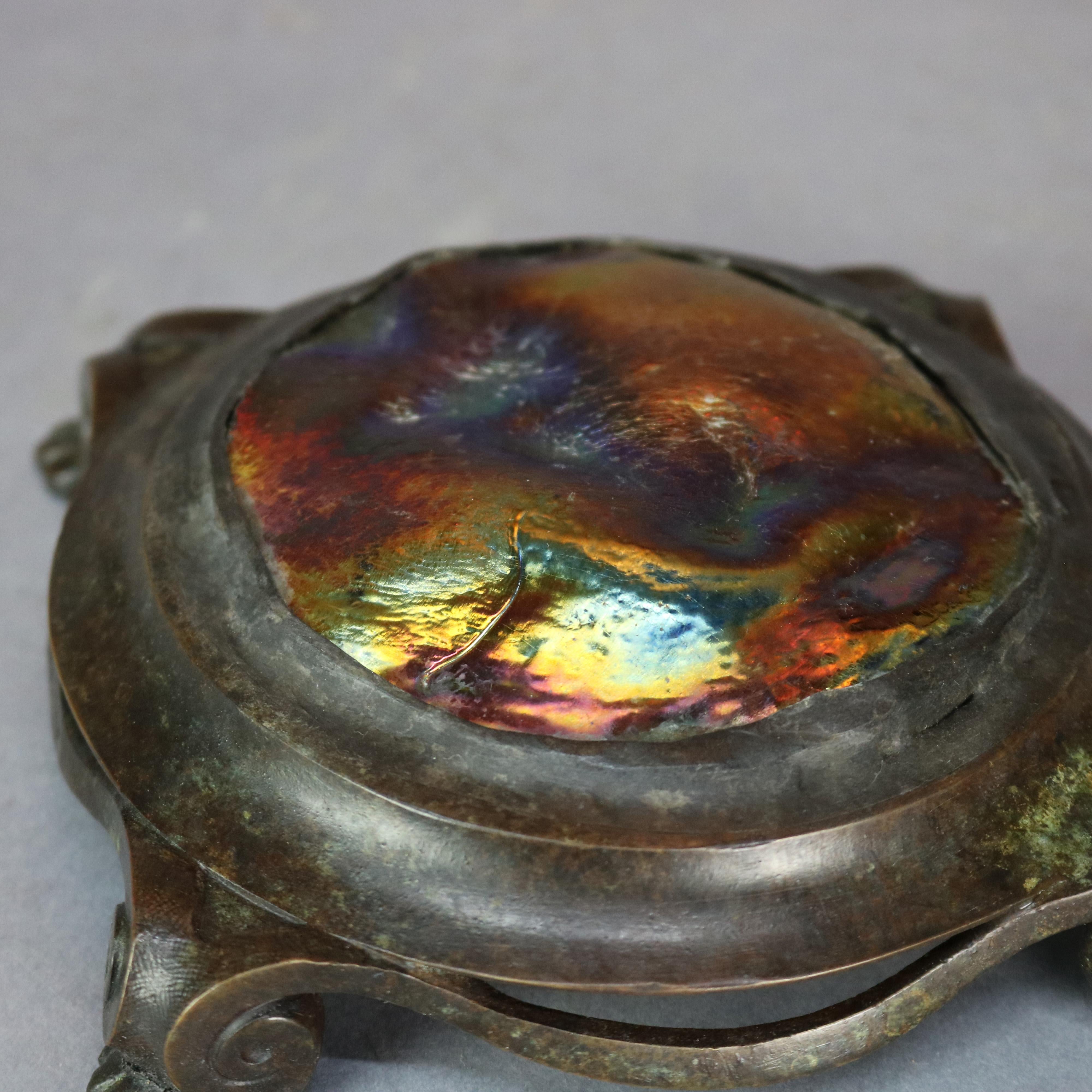 An antique paperweight in the manner of Tiffany Studios offers bronze circular stepped frame having scroll form feet and housing art glass medallion, later added stamp 