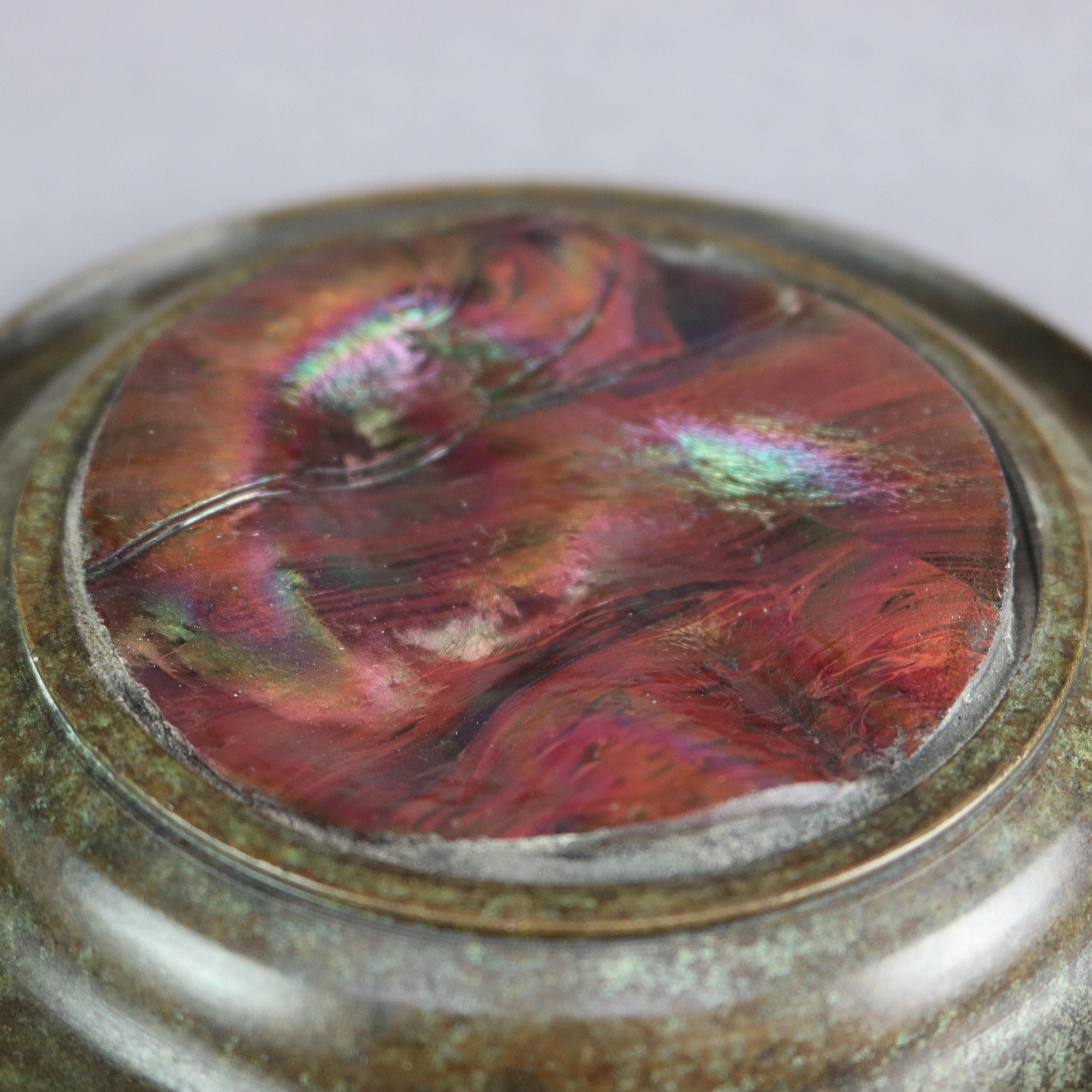 An antique paperweight in the manner of Tiffany Studios offers bronze circular stepped frame having slight well and reeded edge and housing art glass medallion with red tones, en verso later added stamped 