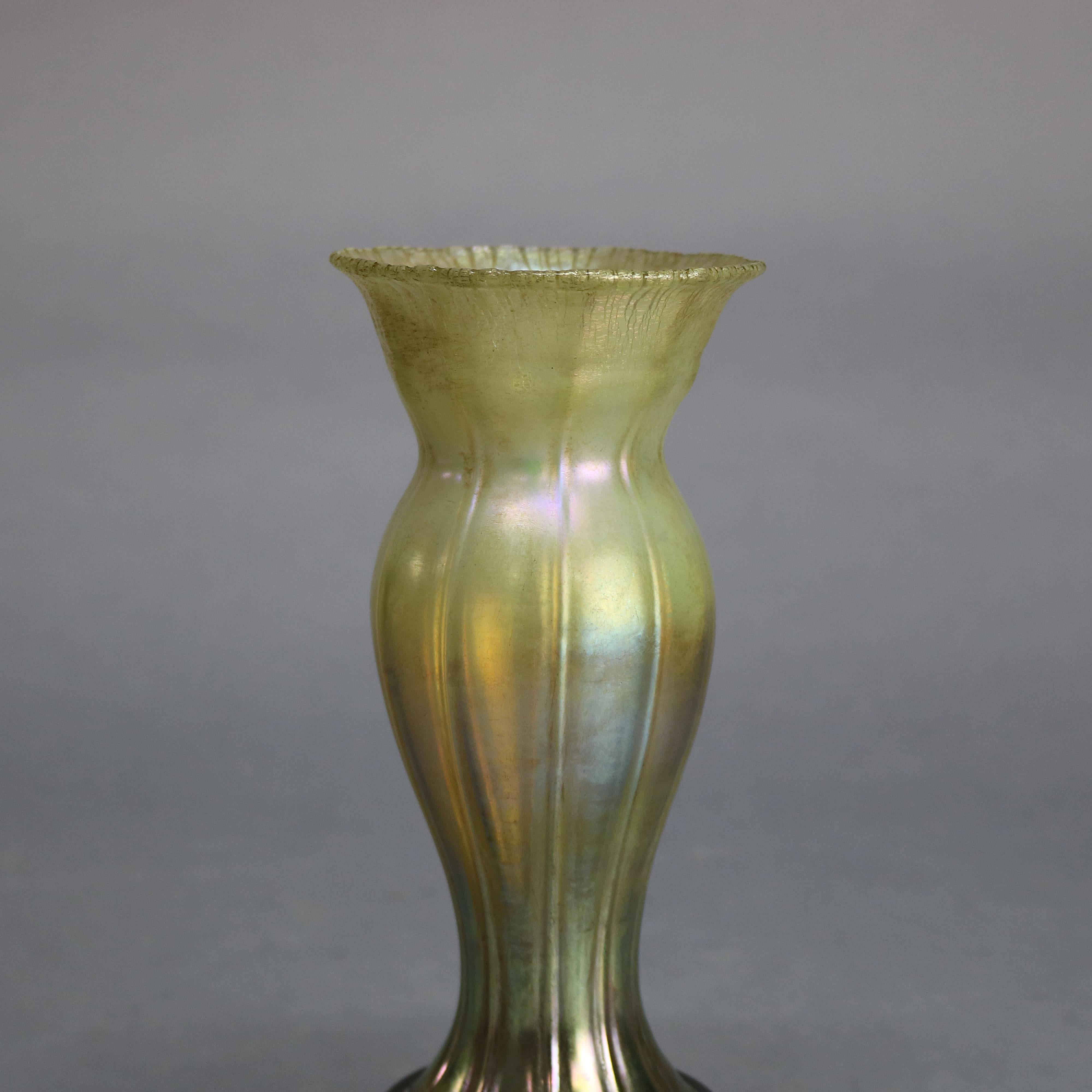 An antique vase by Tiffany Studios offers Favrile art glass silhouette form ribbed vessel seated on cast base with foliate elements, signed on base as photographed, circa 1920

Measures: 9.5