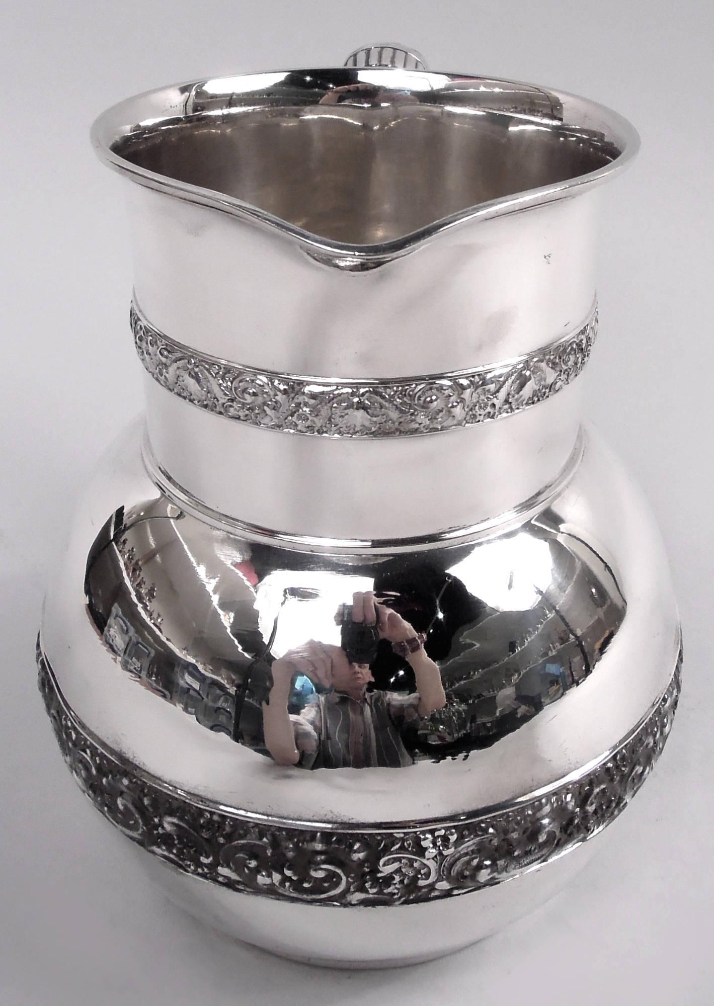 Victorian Classical sterling silver water pitcher. Made by Tiffany & Co. in New York. Globular bowl and drum-form neck with small lip spout; c-scroll handle with ribbed bands. Cast low-relief bands with leafing scrolls and flowers applied to neck