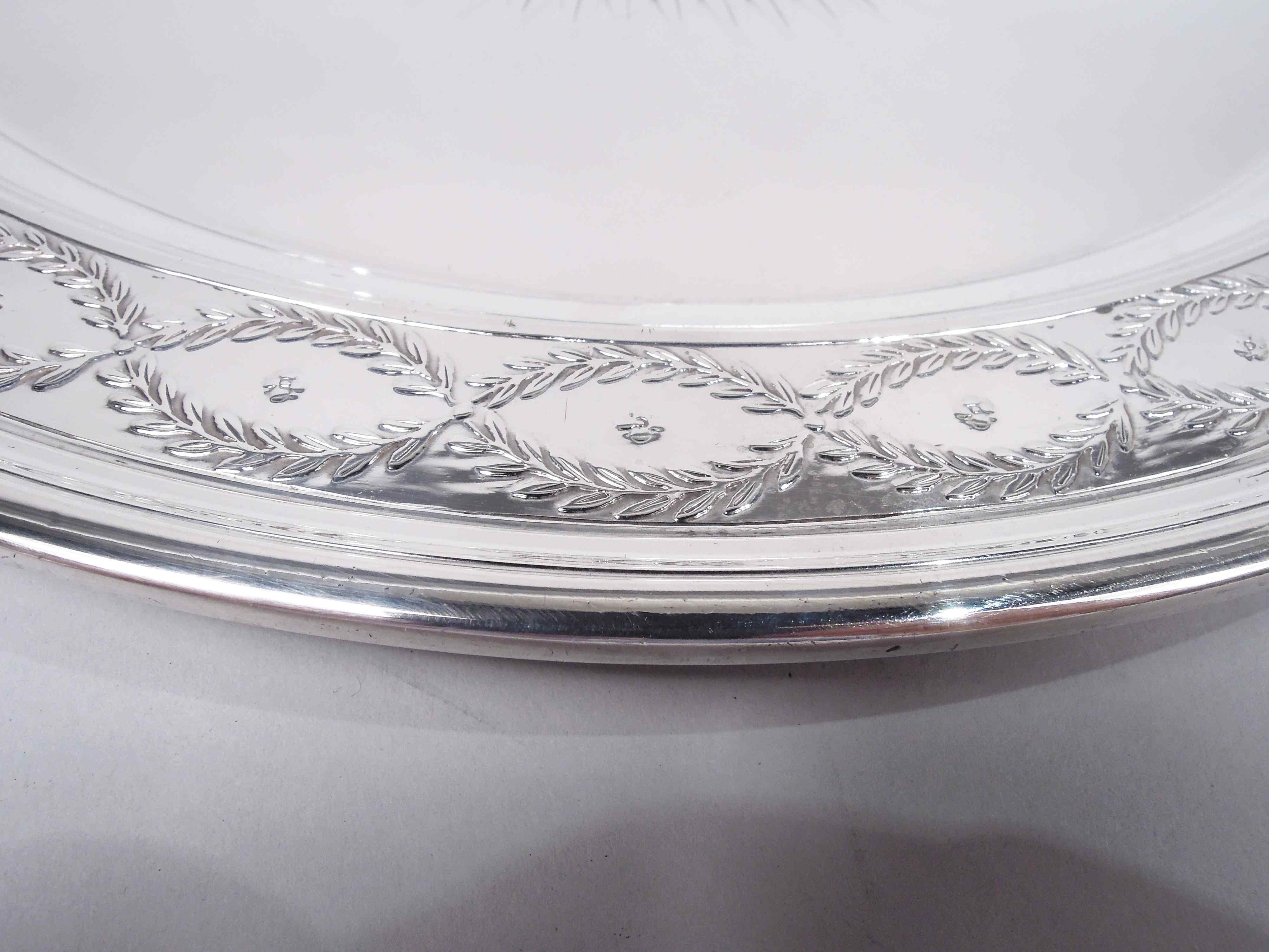 Winthrop sterling silver tray. Made by Tiffany & Co. in New York, ca 1923. Round well with patera comprising beaded rondel (vacant) radiating leaf-and-dart. Shoulder flat and tapering with laurel wreaths inset with flower heads. Ornament