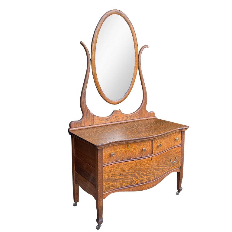 A stunning tiger oak wood dresser with an oval mirror. Sourced from an estate in Kansas, this gorgeous wood piece has fabulous grain. The piece could be used as a dresser, dressing table, or vanity. The top is low, with a serpentine top. There are