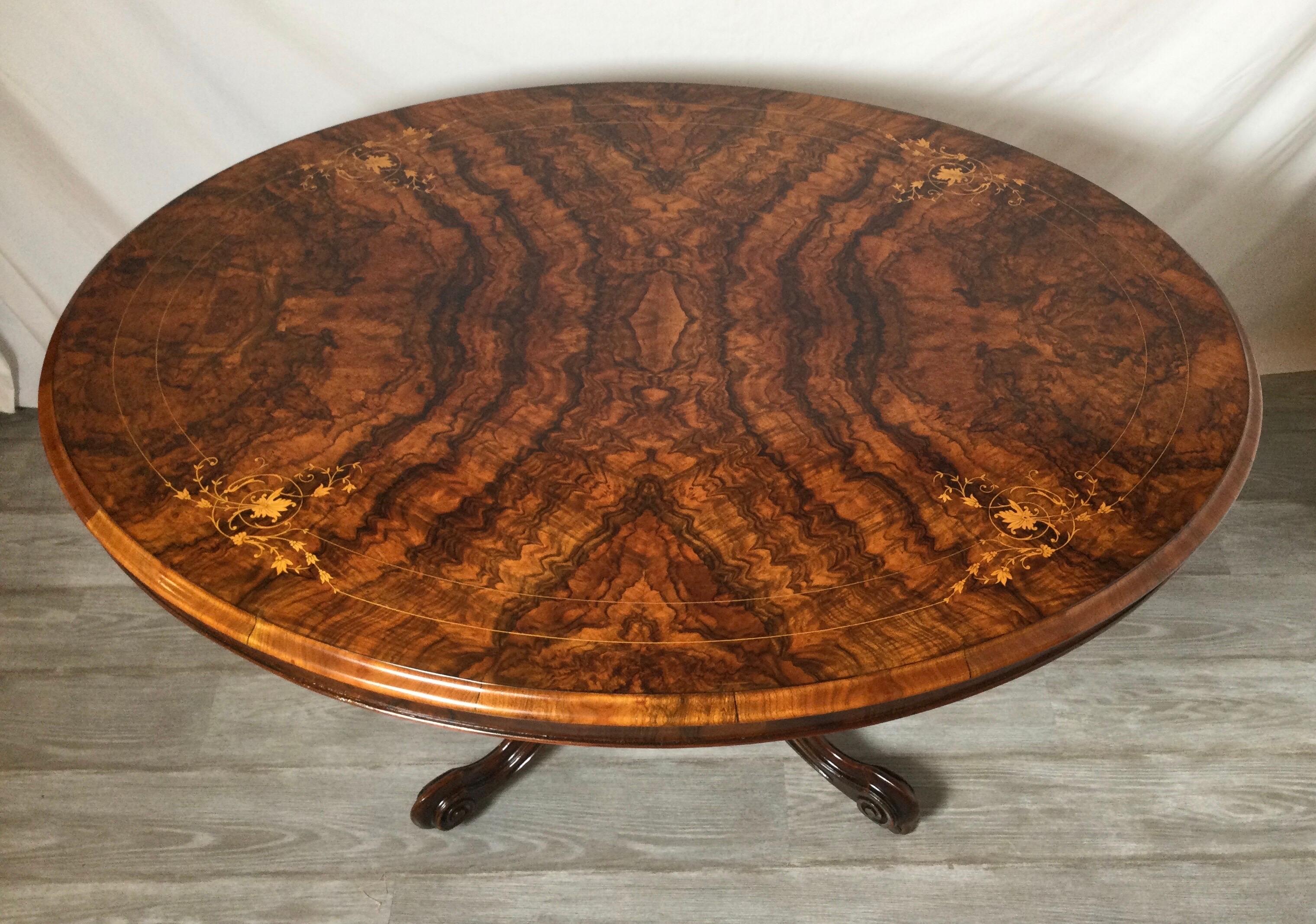 An oval walnut breakfast table with hand carved pedestal base. The highly figural burl walnut with inlay of satin wood. The top tilts to allow easy moving around and storage.