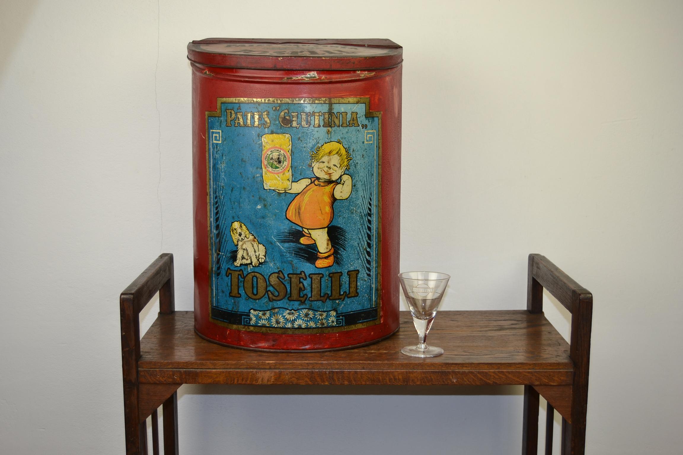 Cute looking large tin for Italian Pasta Toselli.
This grocery tin, storage tin has a Lithographic design:
a cheeky laughing girl holding a pack of pasta and next to her a sitting dog which is looking angry.
All on a blue background and on a red