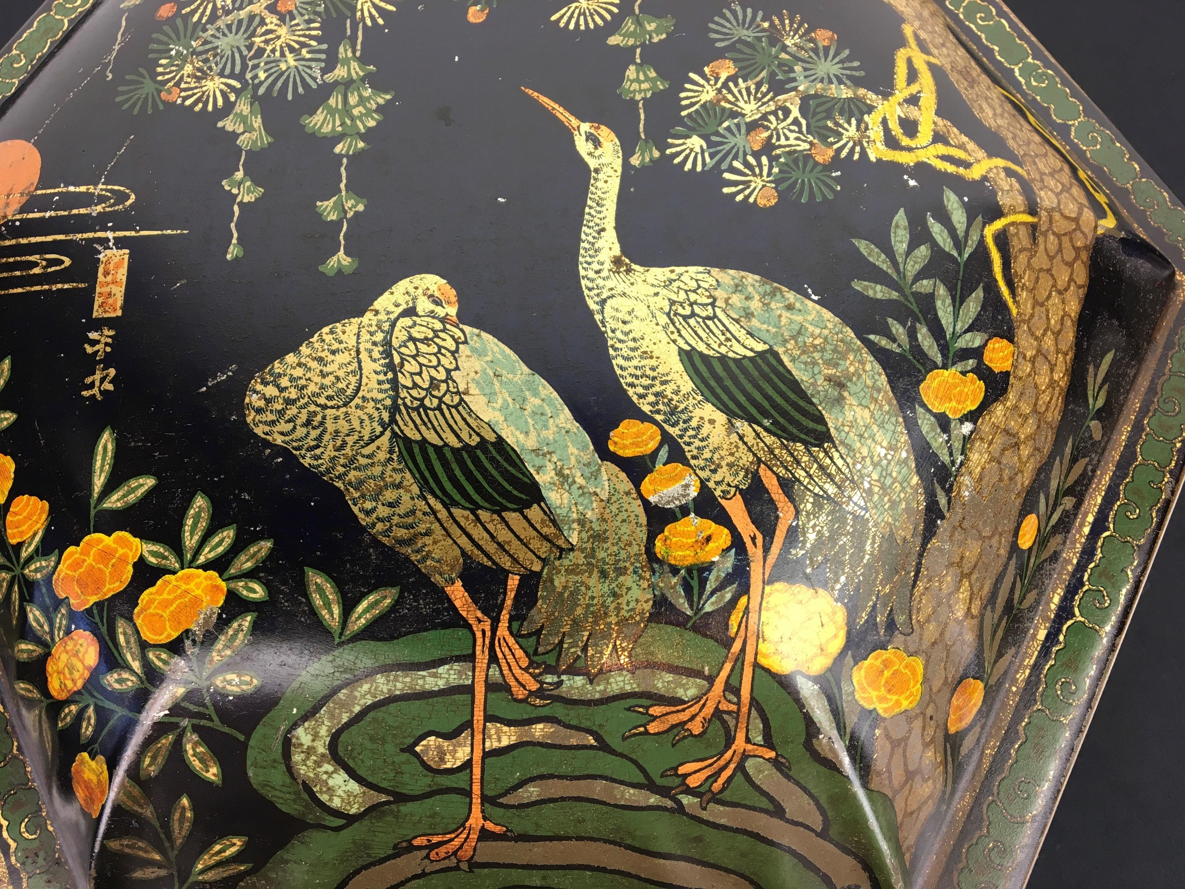 Antique tin in Asian style with cranes. 
This lithographic tin box with birds dates from the early 20th century.
It's a stylish and elegant antique metal storage tin in hexagonal shape with lid.
In dark blue color with a beautiful design in Asian