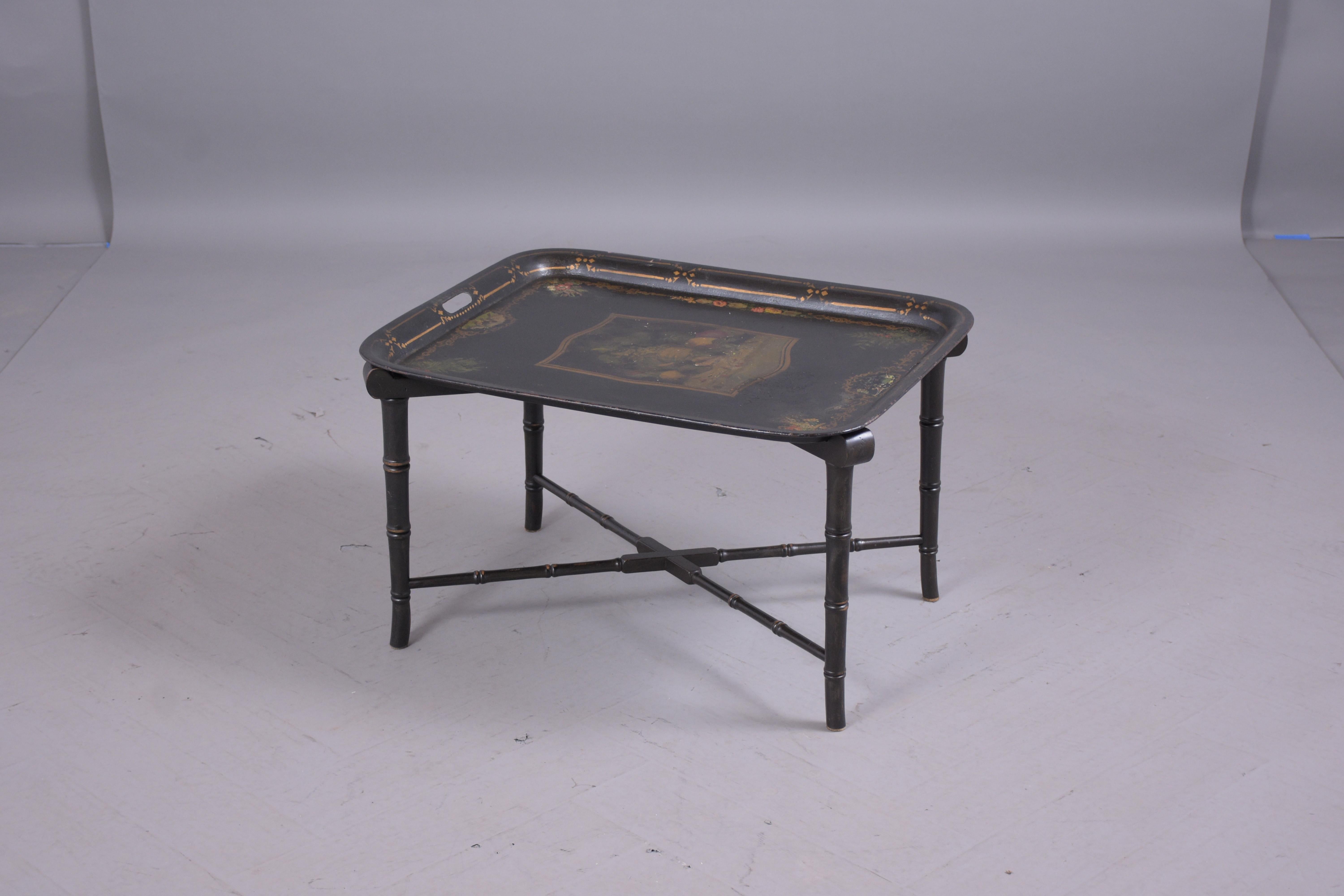 An extraordinary 1900s tole tray table, the top is crafted of metal, features trim details around the tray a fruit basket in the center. The top sits on a vintage wood base with faux bamboo design with its original ebonized finish, only cleaned and