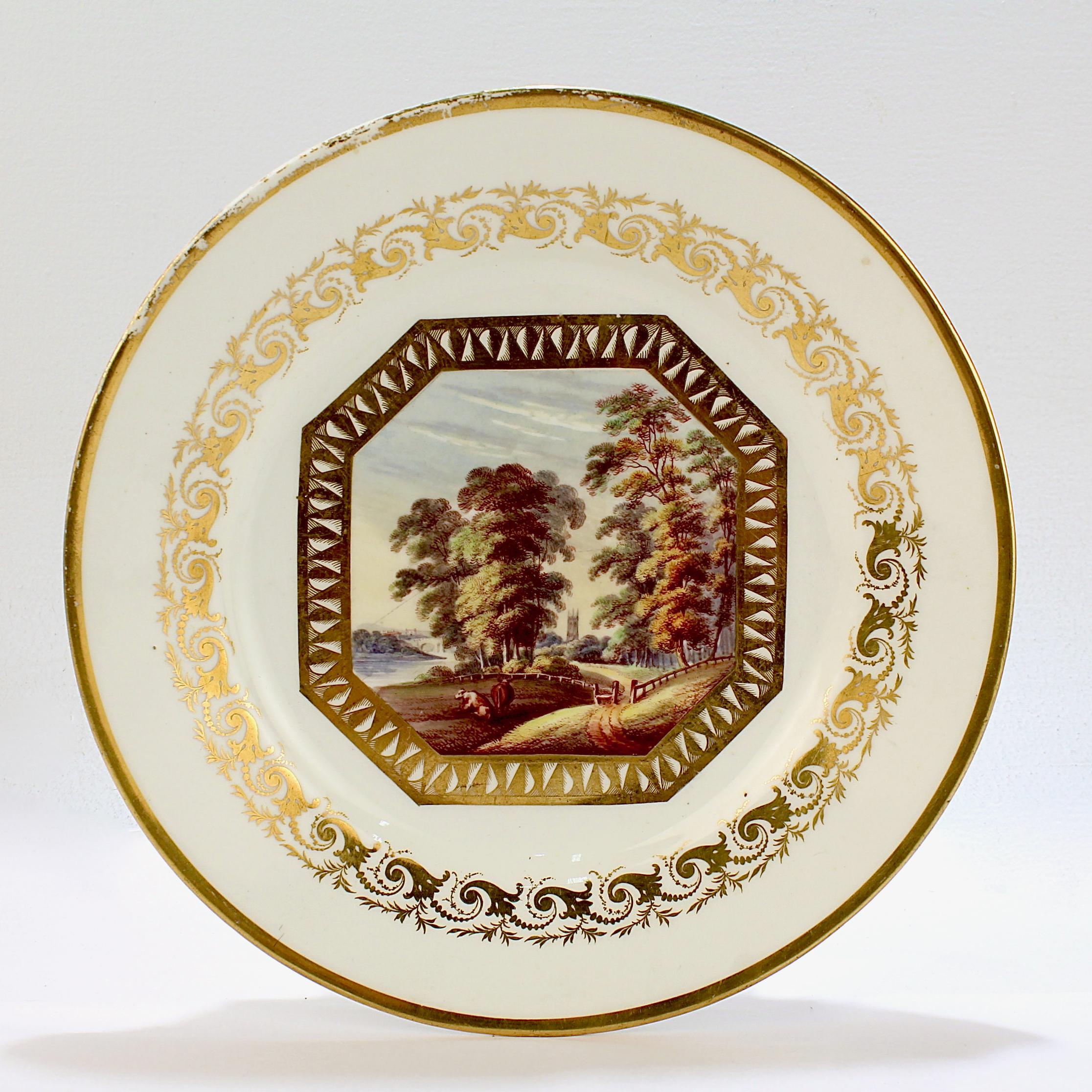 A fine antique 19th century Derby hard paste porcelain plate.

Decorated with a hand painted topographical scene to its center.

The scene depicts a bucolic landscape 'Near Derby' in a gilt cartouche and surrounded by a gilt cornucopia design.