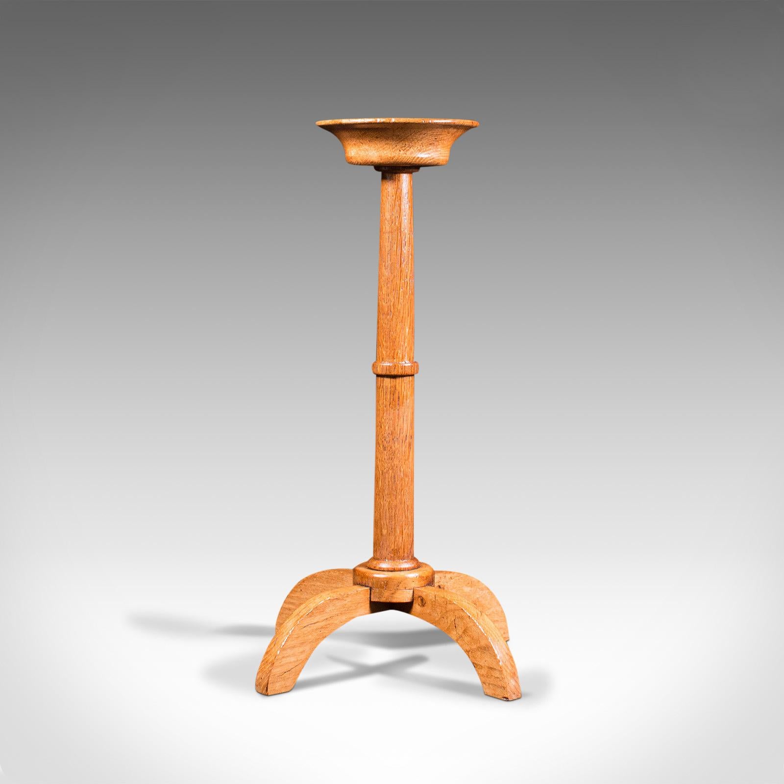 This is an antique torchere. An English, oak candle stand in the manner of the Cotswold school or Arts & Crafts movement with ecclesiastical overtones, dating to the early 20th century, circa 1920.

Appealing light oak hues and attractive