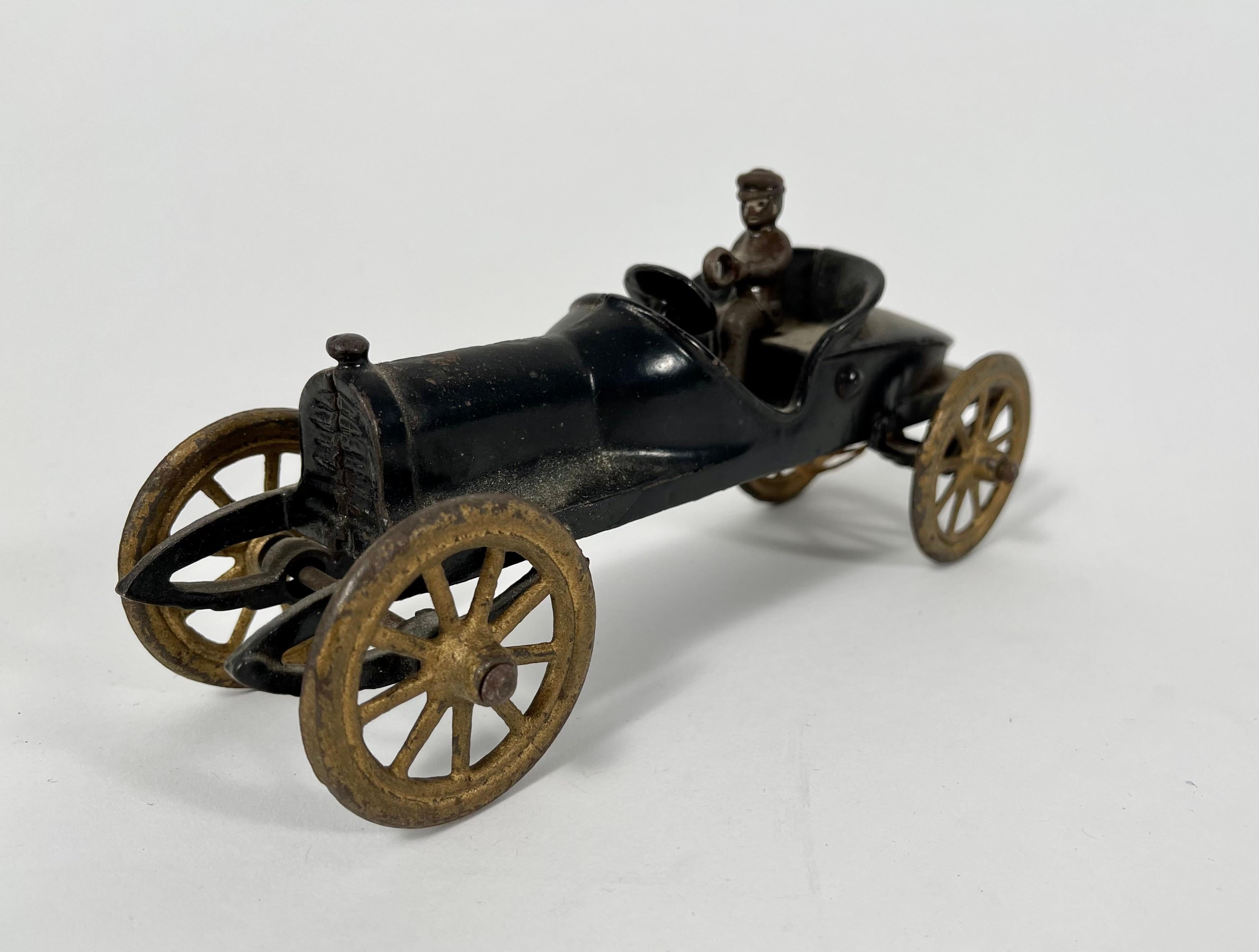 A vintage black painted metal toy race car, circa 1920s with associated removable driver.