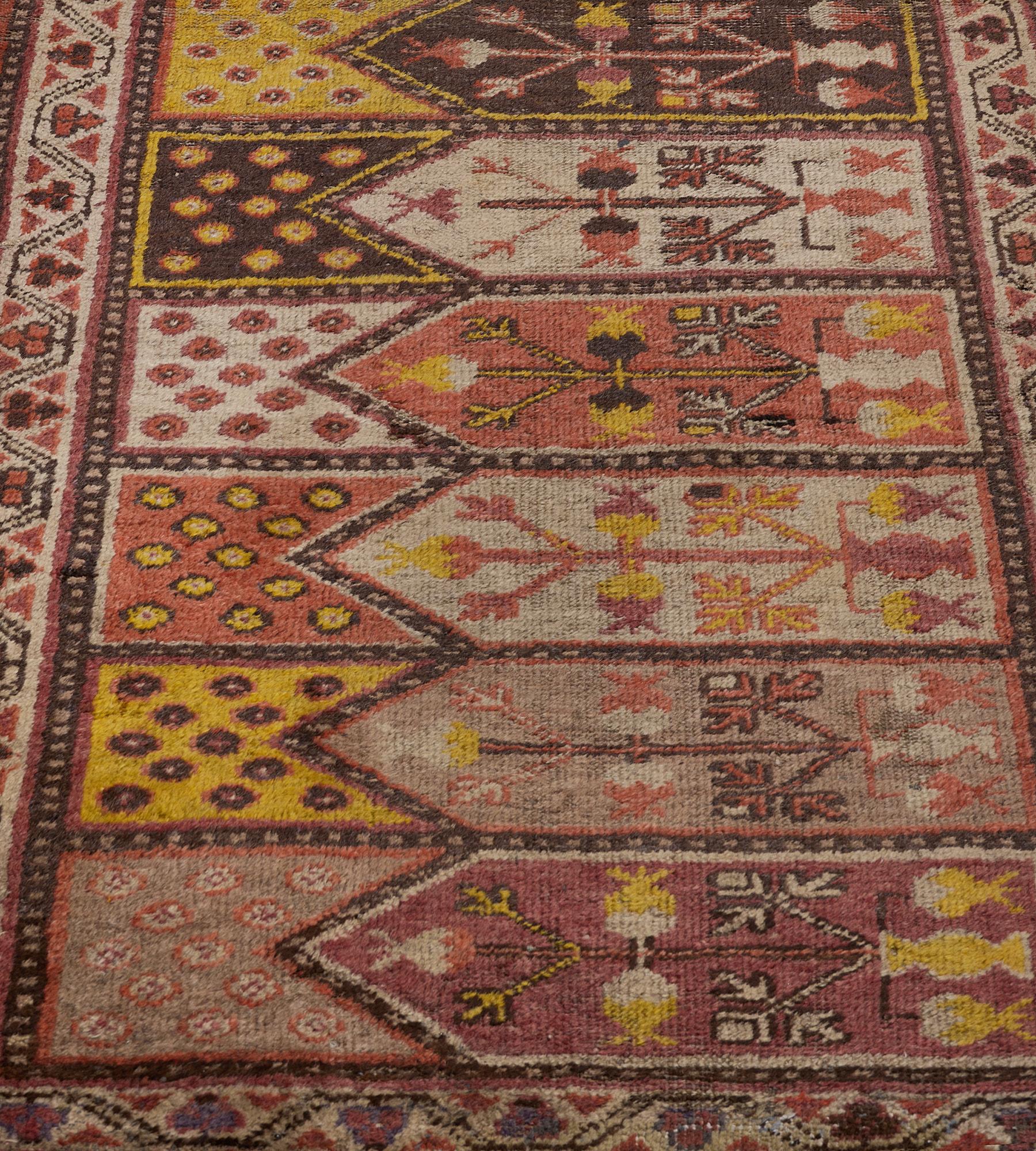 This antique, hand-woven Khotan runner has a field with horizontal polychrome panels each with a vase issuing angular pomegranate and floral motifs, the arched polychrome panels above with small flowerheads, surrounded by a narrow chocolate-brown