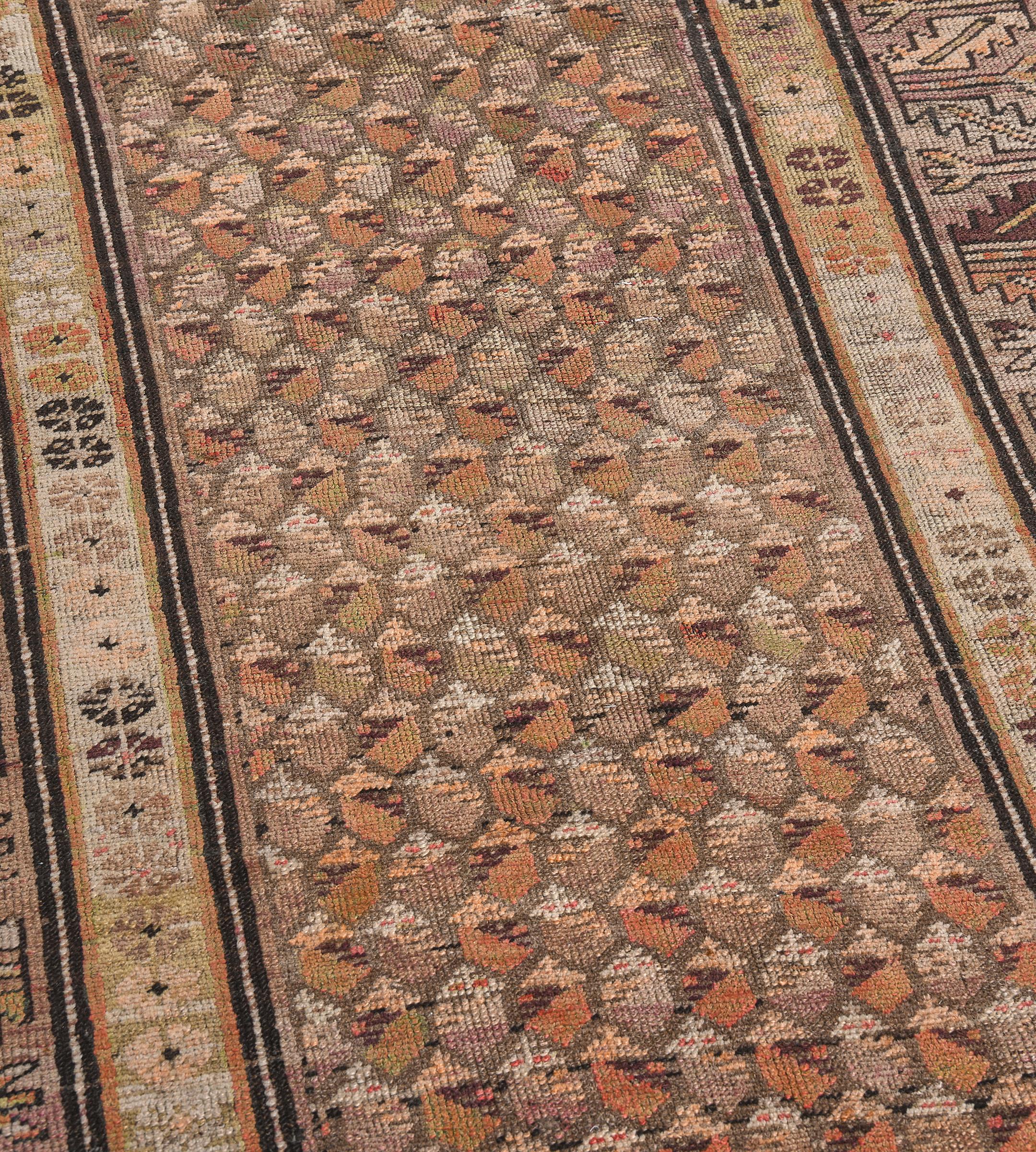 This traditional hand-woven Persian Karabagh rug has a shaded tobacco field with an overall copper paisley pattern, in a broad shaded tobacco serrated leaf border, between shaded sandy cream geometric rosette stripes.