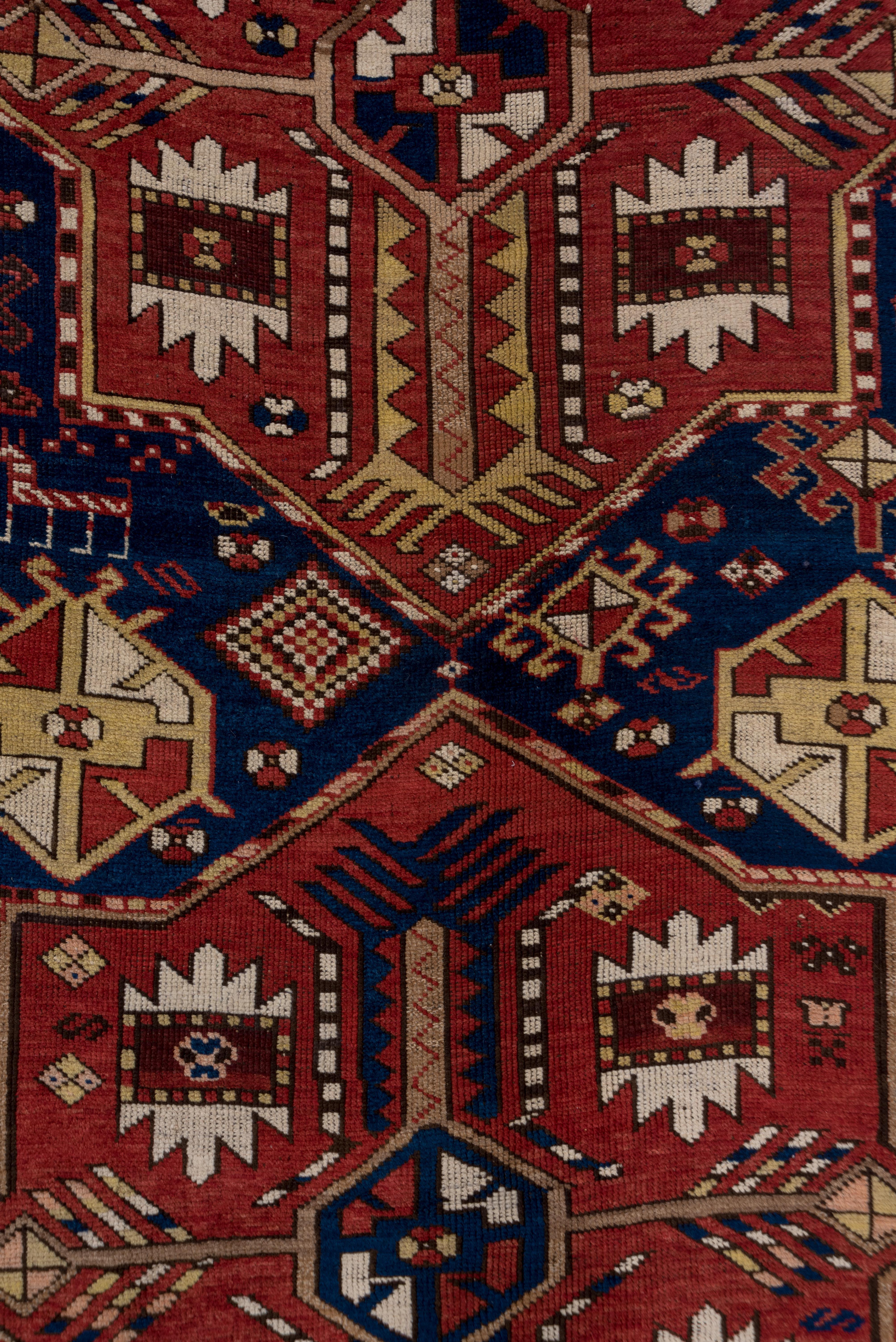 This antique Transcaucasian rug features a dynamic shield medallion design in a rich blend of crimson, indigo, ivory, and ochre tones. The field is energized by a bold arrangement of geometric medallions and stylized elements, evoking tribal