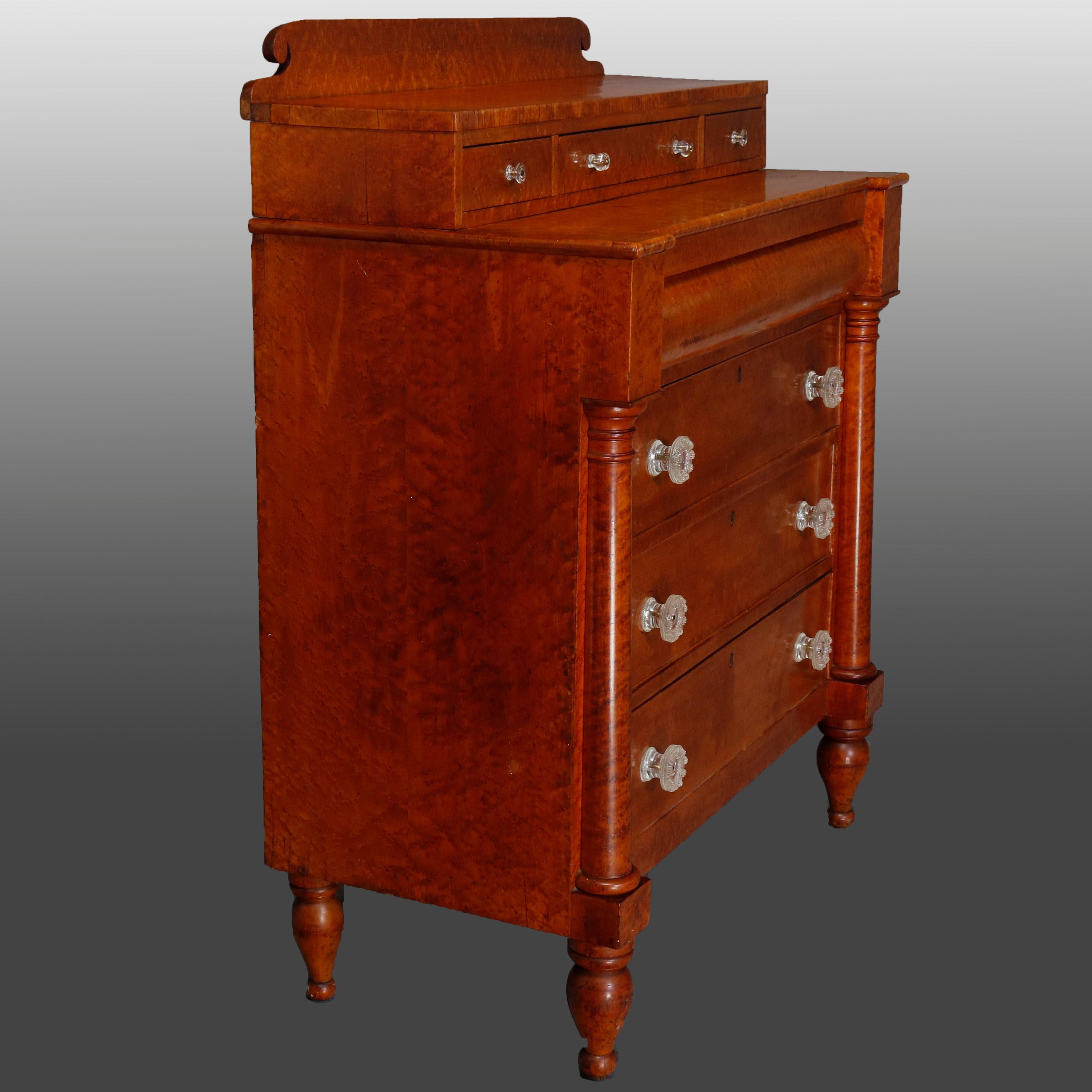 An antique Transitional Empire to Sheraton chest of drawers offers bird's-eye maple construction with top having shaped backsplash over three smaller drawers surmounting chest having upper convex frieze drawer over three long drawers with sandwich