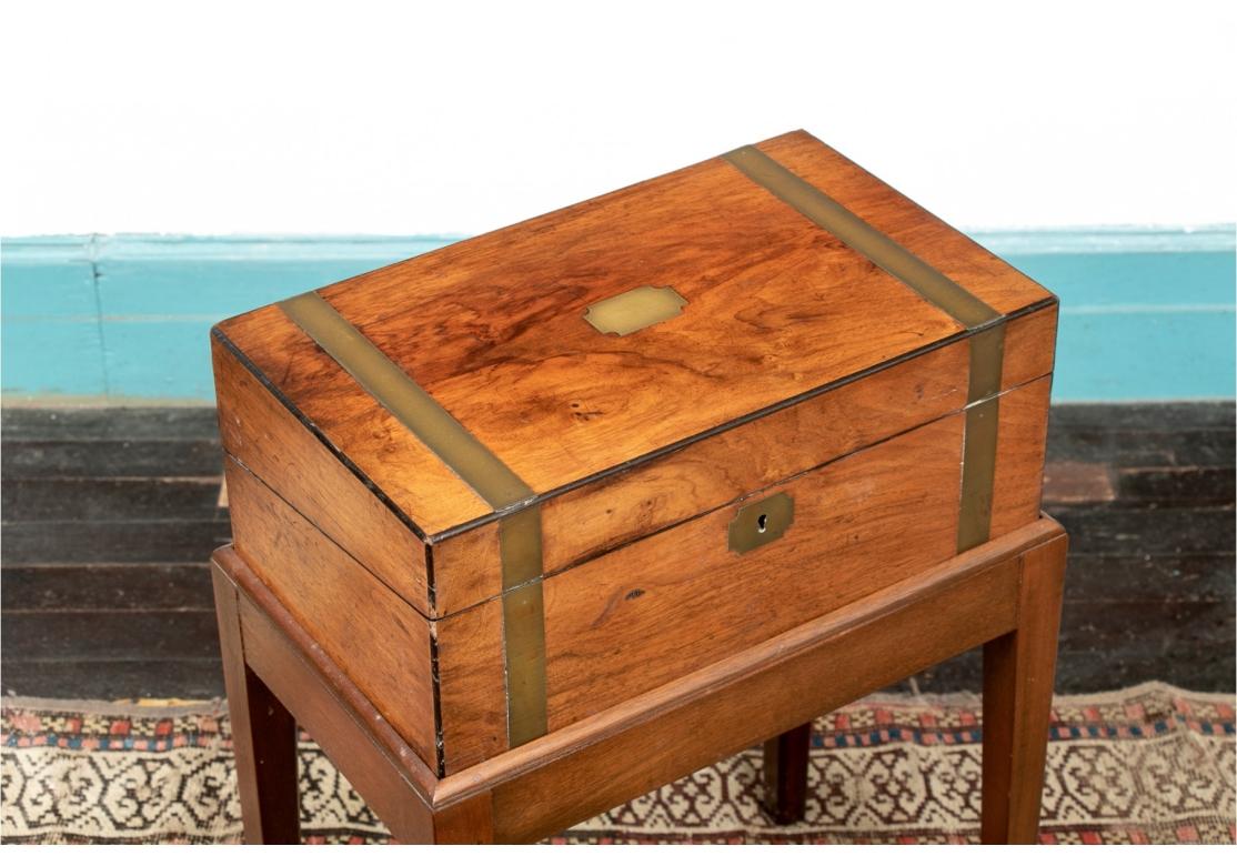 Antique travel desk with brass bands, tooled leather interior, brass shield plate and escutcheon, ebonized trim and presented on a plain stand with tapering legs.

Dimensions: 15 3/4