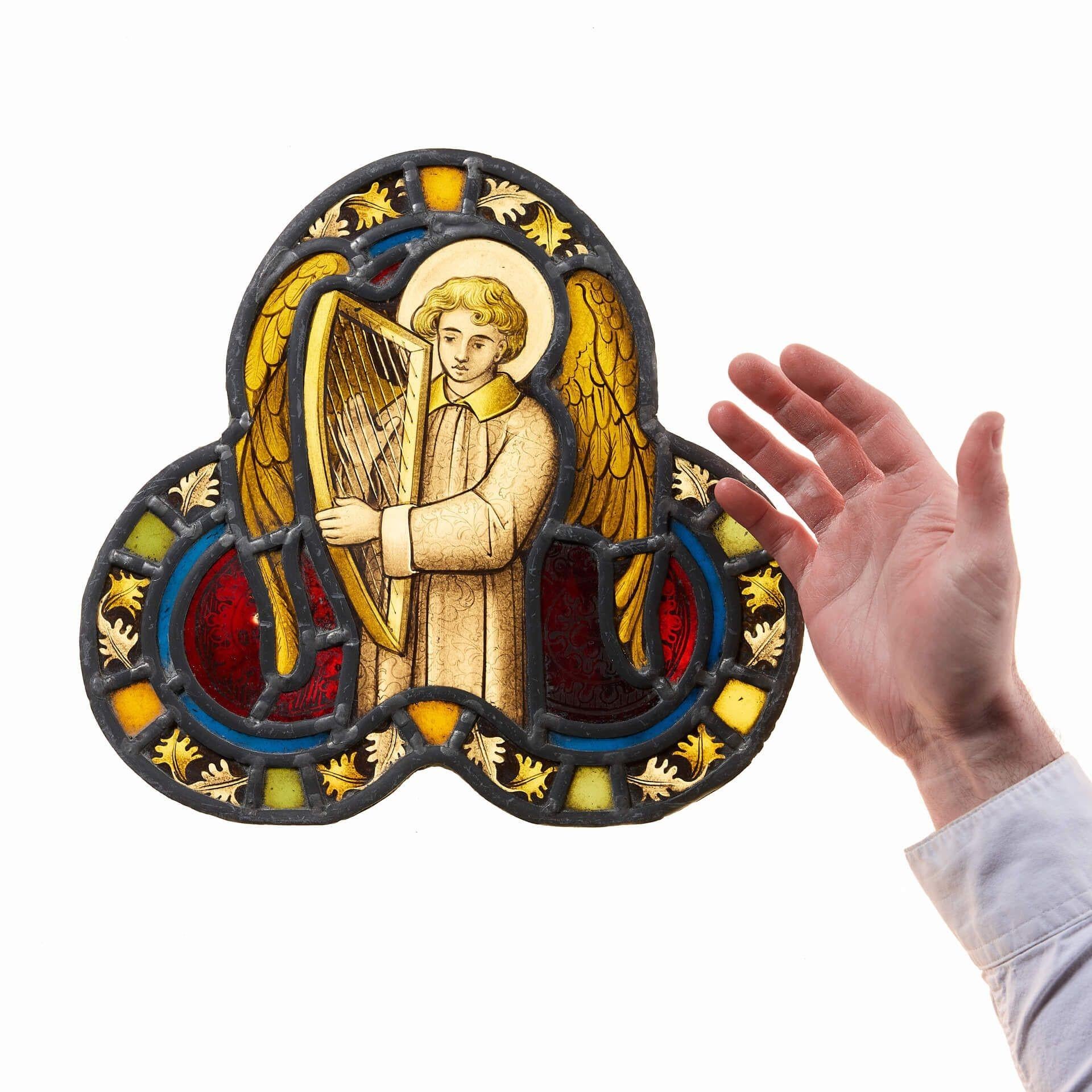 Un petit vitrail tréflé ancien bien capturé, vers 1880.

Ce vitrail représente un ange aux cheveux blonds bouclés, vêtu d'une robe classique, les ailes dorées déployées, jouant de la harpe, entouré d'une bordure de feuillage aux teintes jaunes et